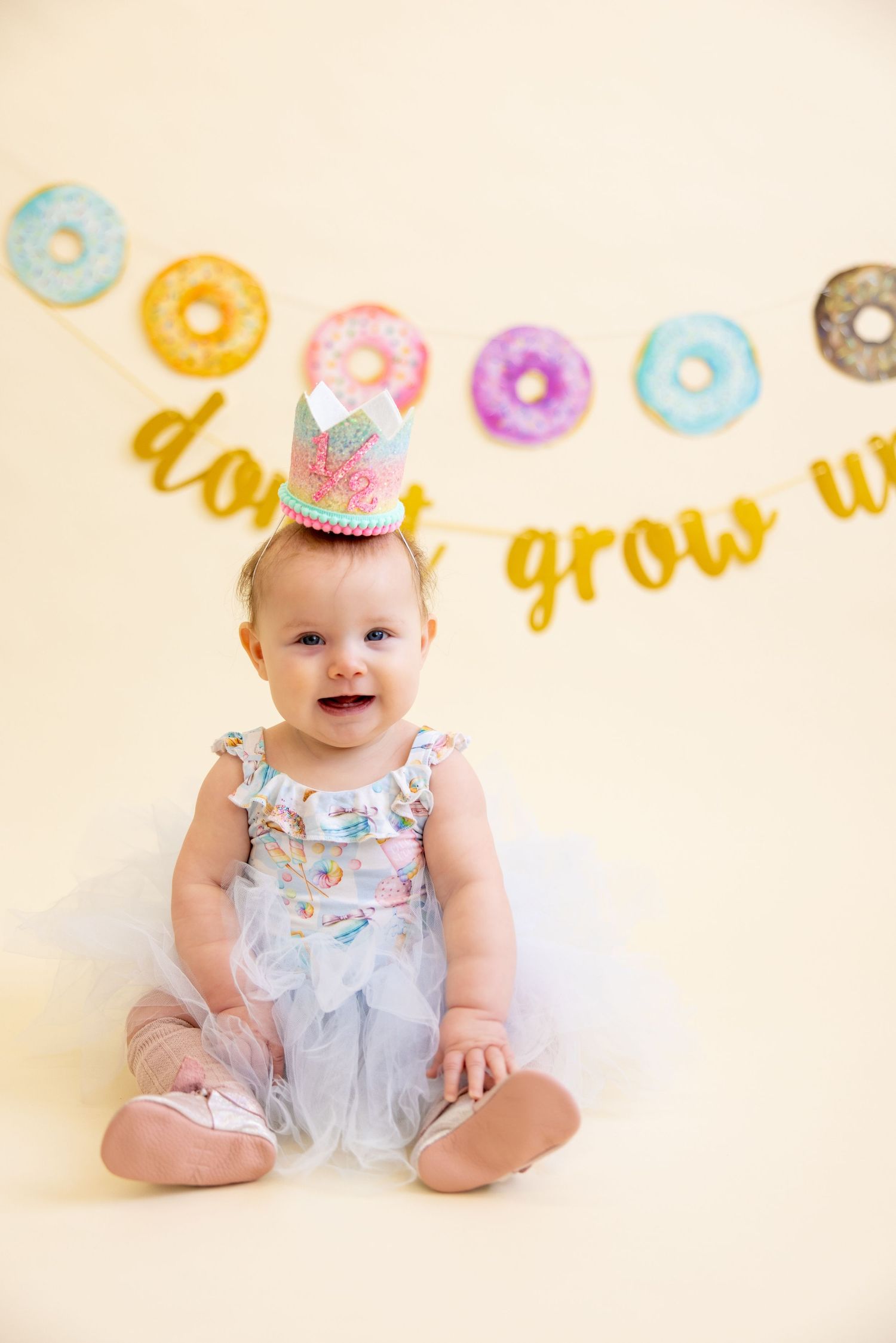 Baby wearing party hat sits under donut-themed banner with colorful decorations.