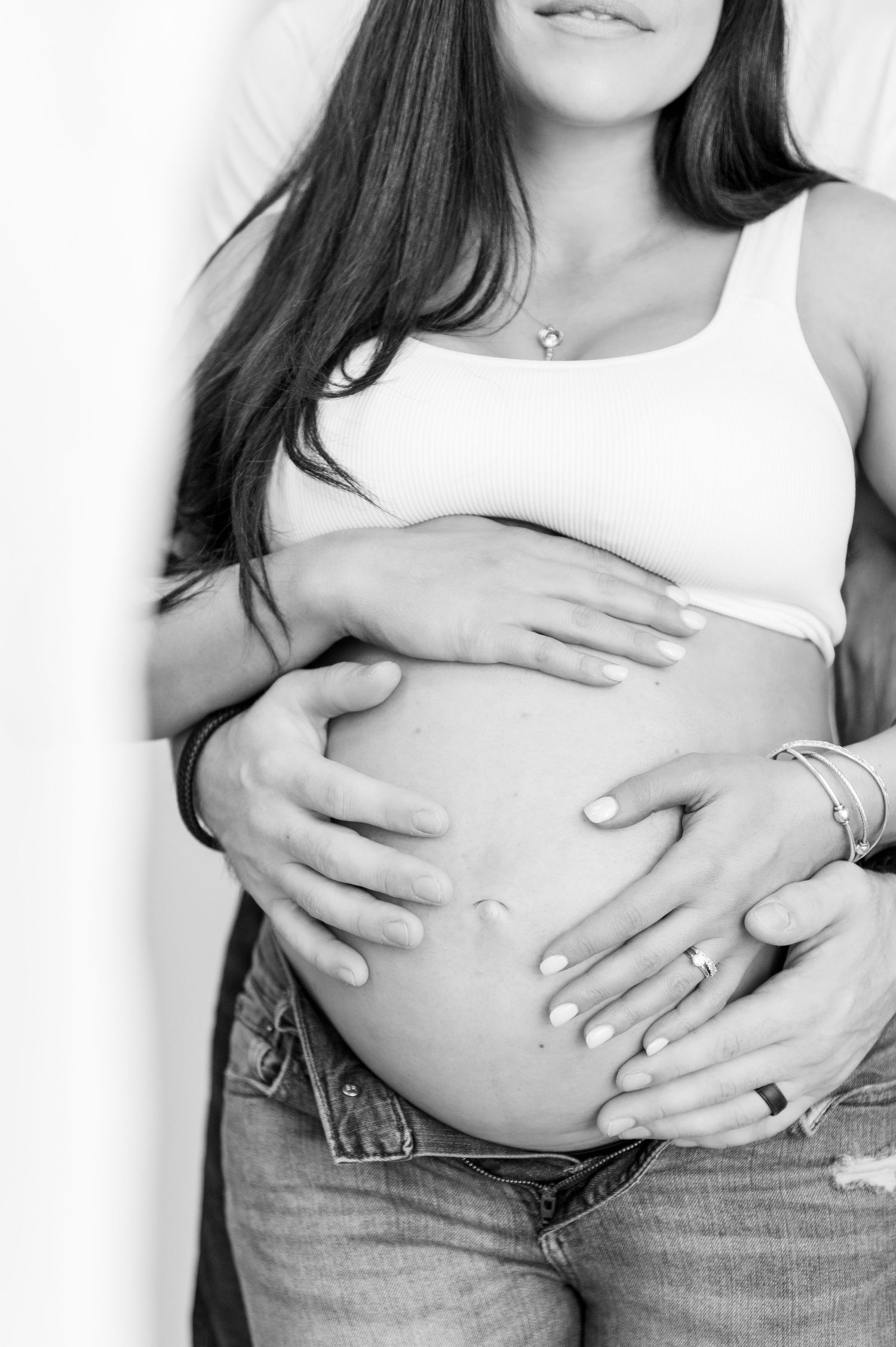 Black and white close-up of pregnant belly with hands tenderly placed on bump.