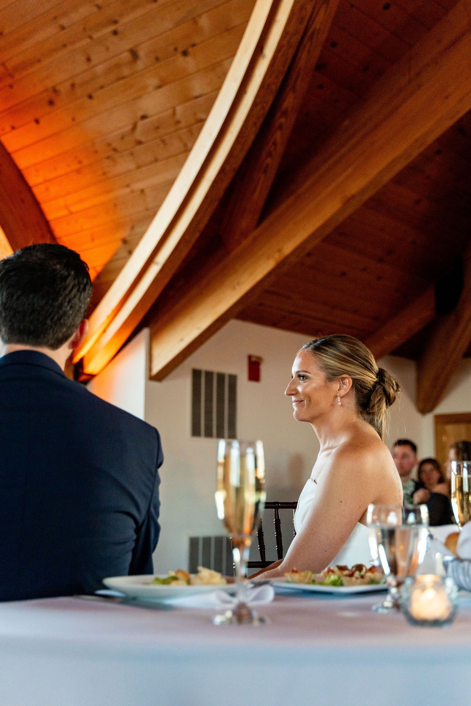 Elegant wedding reception dining setup under wooden beam ceiling with warm lighting.