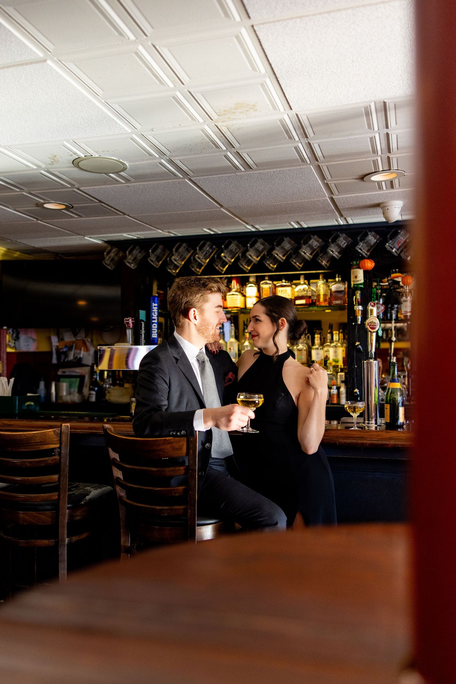 Romantic couple shares drinks at bar counter with ambient lighting.