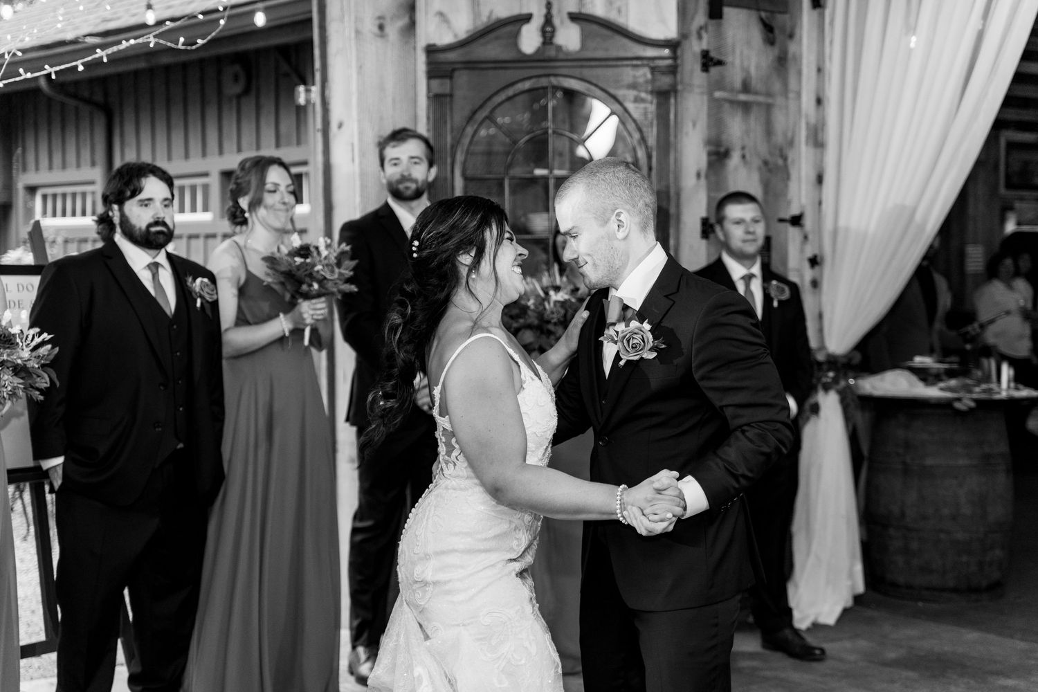 A couple shares their first dance at a rustic barn wedding reception surrounded by guests.