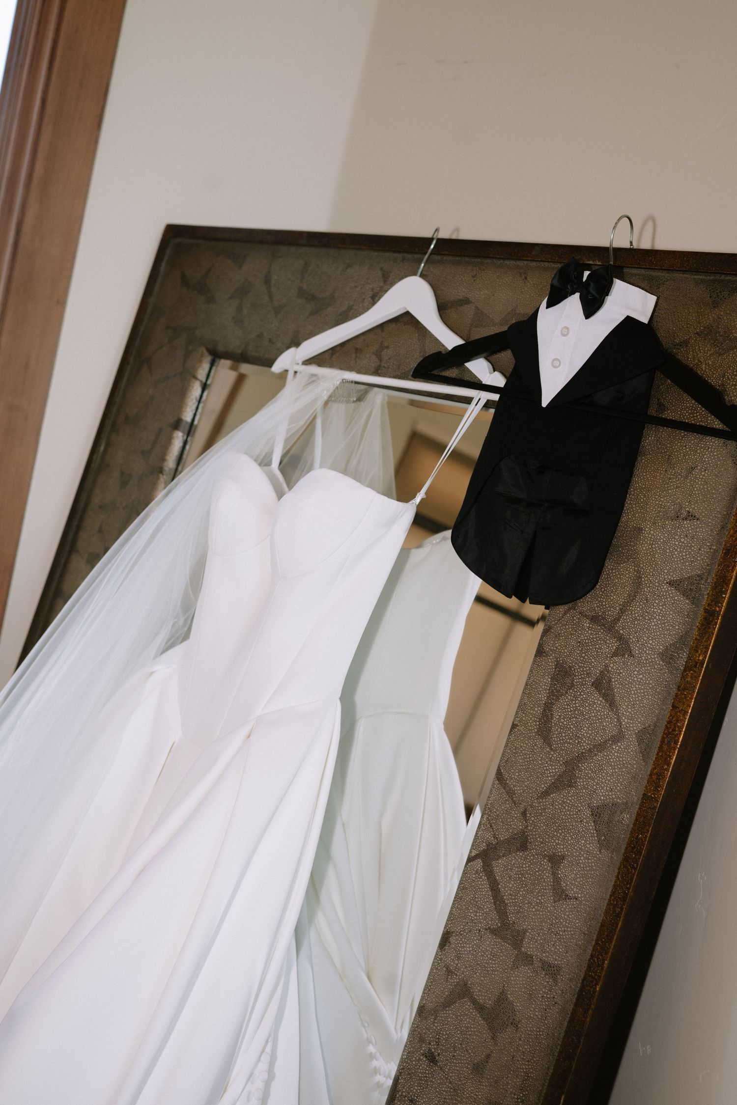 White wedding dress and black tuxedo hanging side by side on hangers.
