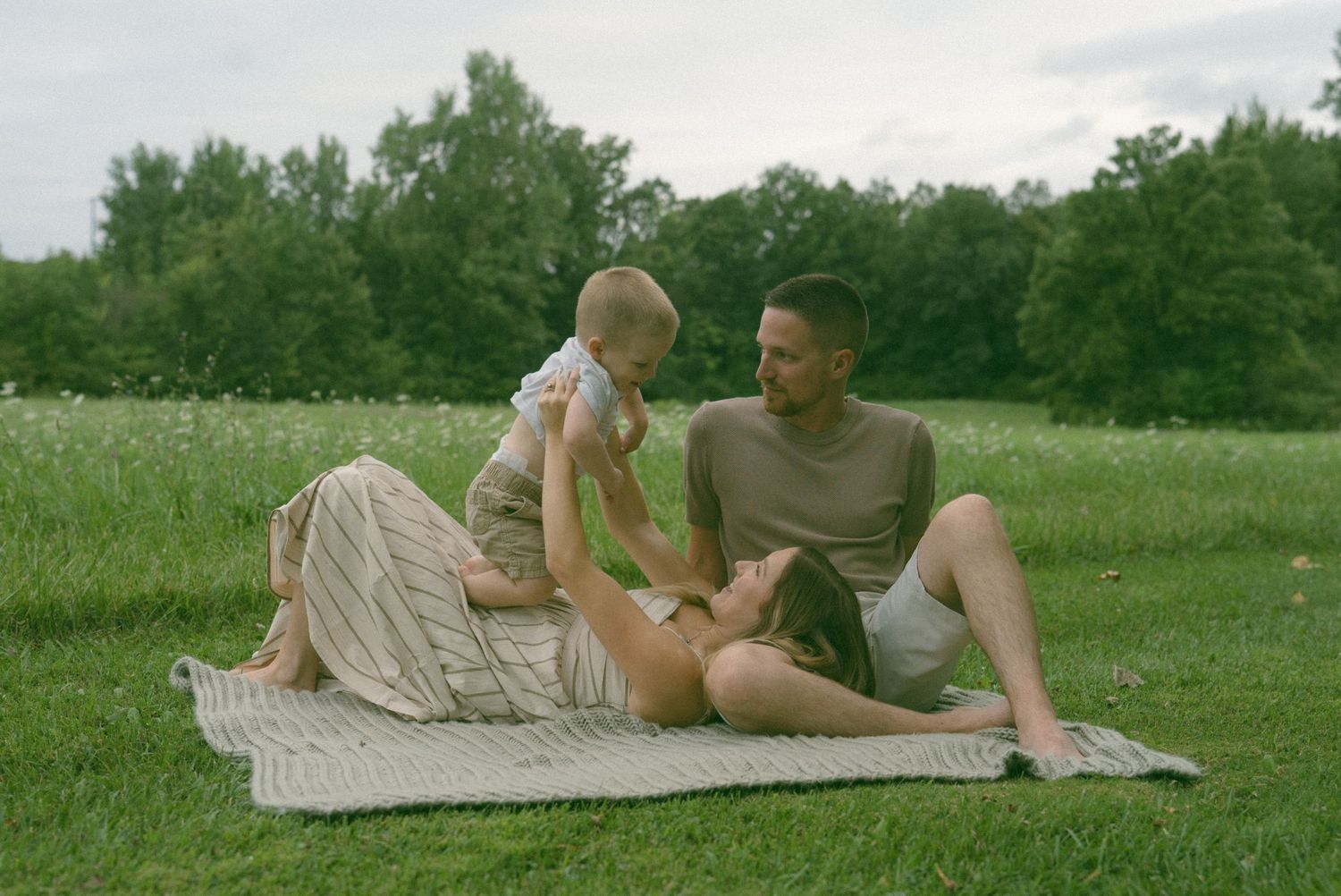 A tender family moment shared on a blanket in a peaceful meadow setting.