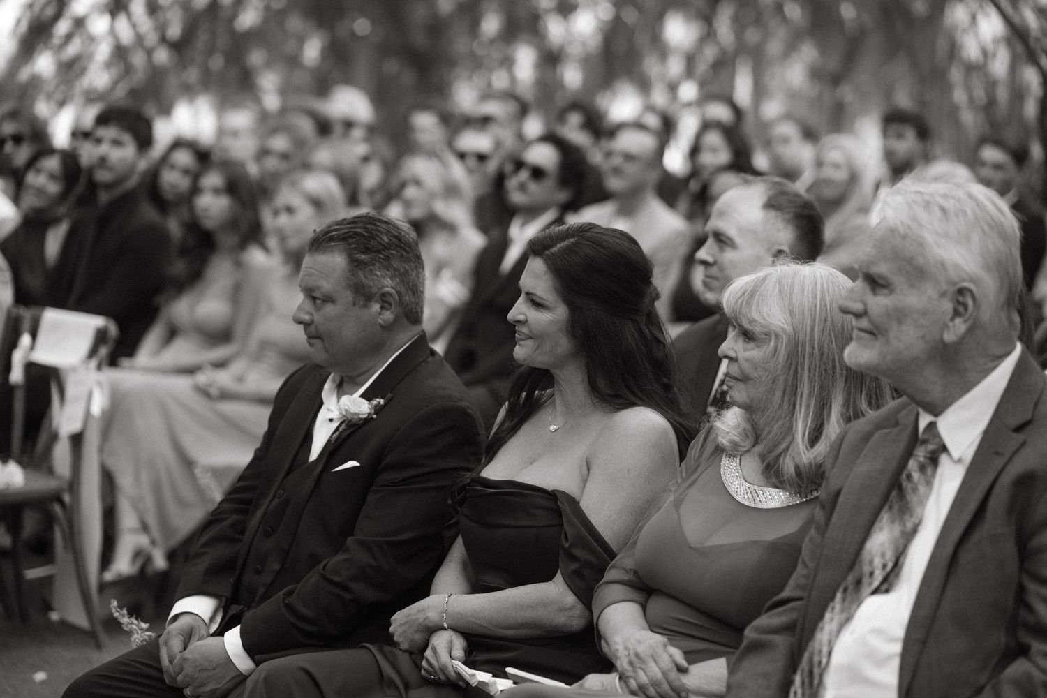 Wedding guests seated outdoors watching the ceremony in black and white photography.