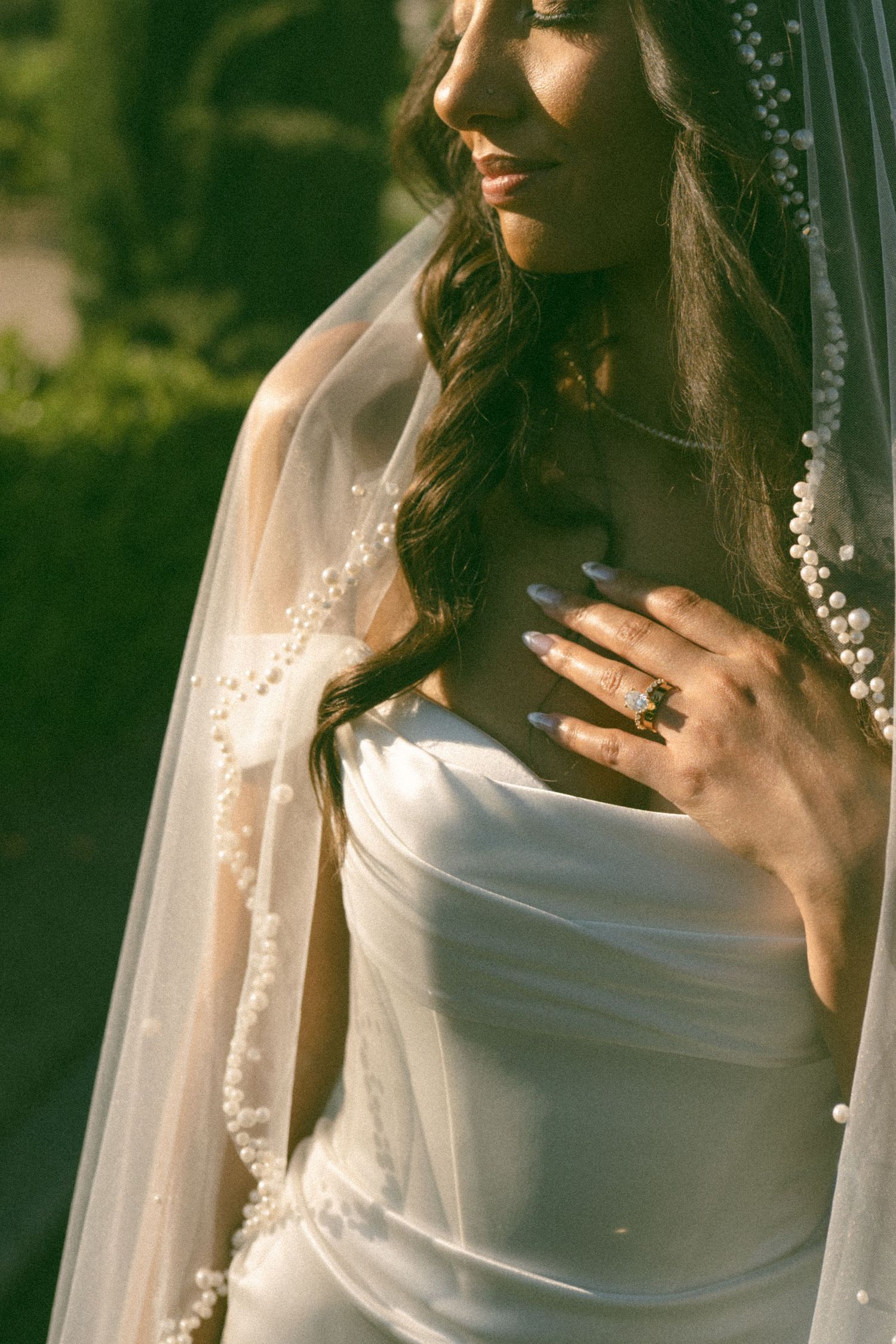 Close-up detail of pearl-adorned wedding veil and engagement ring in warm sunlight.