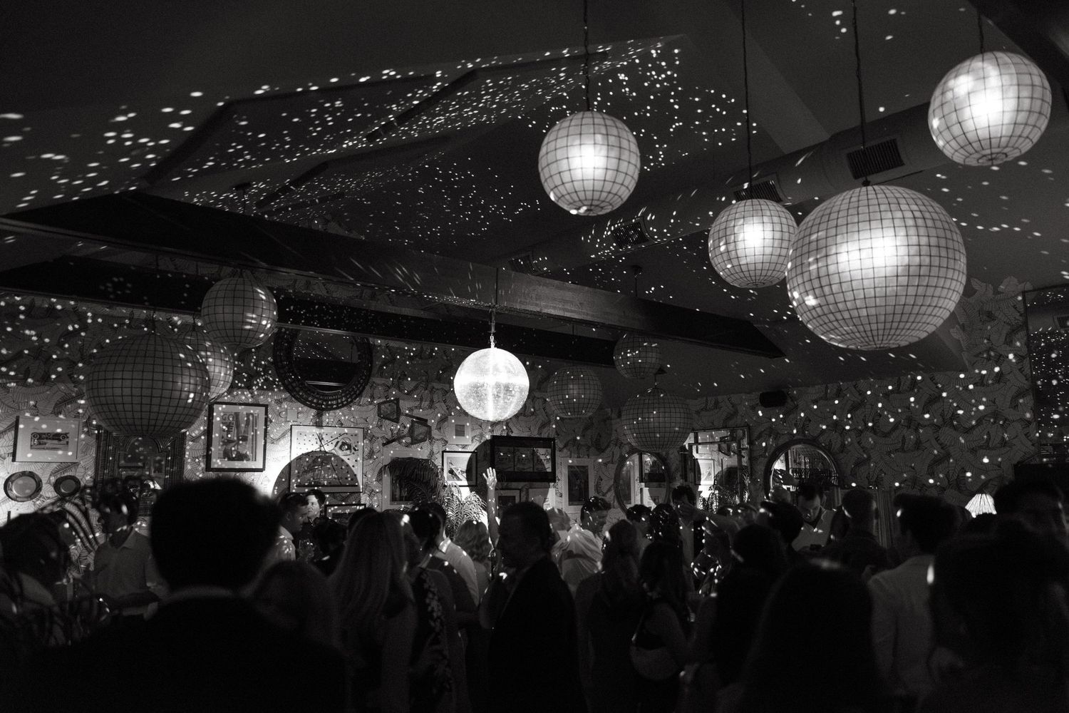 A crowded wedding venue with illuminated disco balls and twinkling lights overhead.
