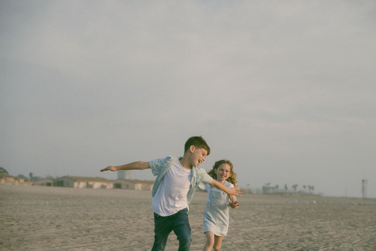 Family members run and play together on an open beach with buildings in the distance.