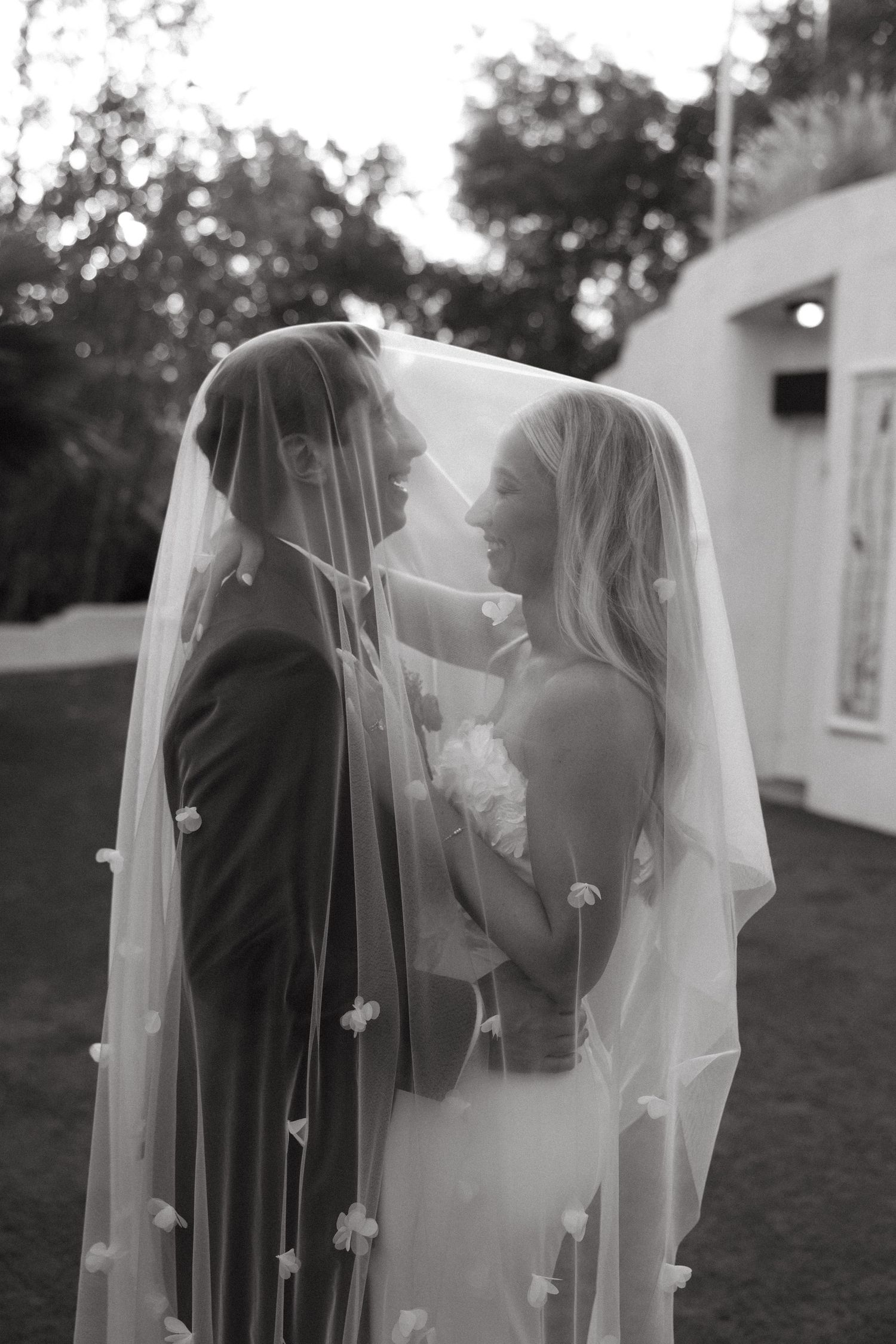 Romantic black and white wedding photo with flowing veil in an outdoor setting.