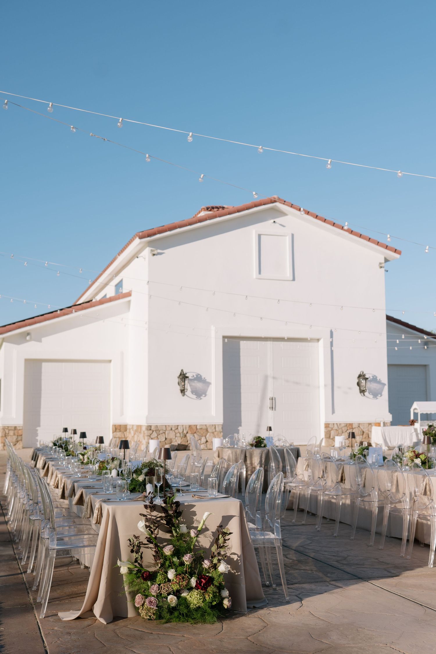White reception venue with string lights and elegant table settings for outdoor wedding.