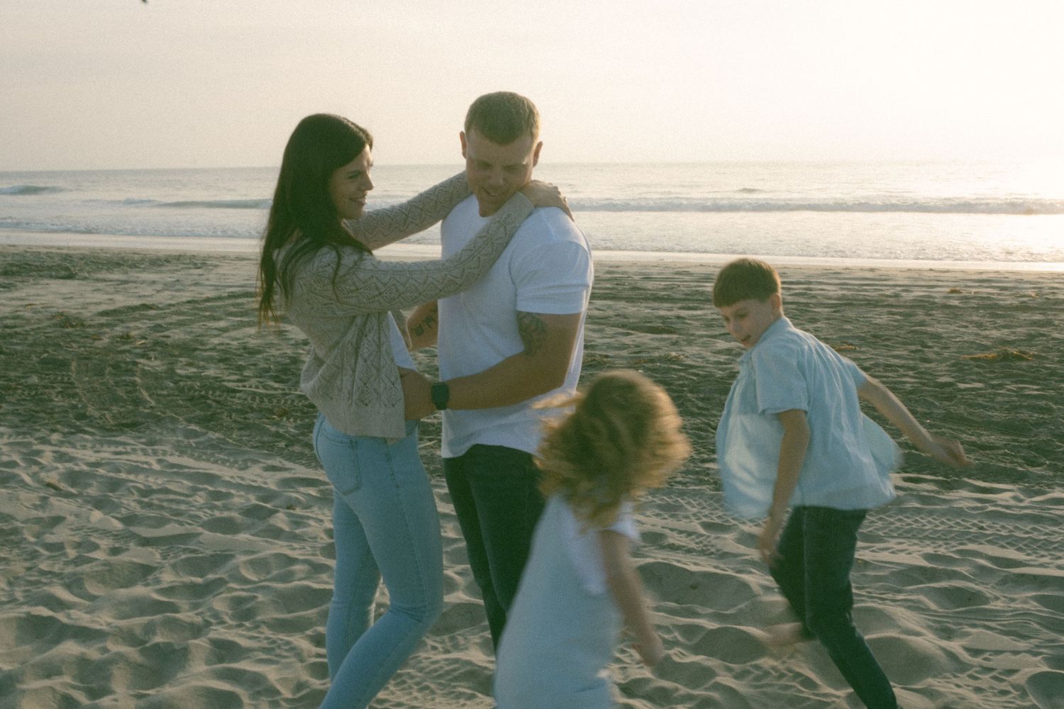 People walking and playing together on a sandy beach at sunset.