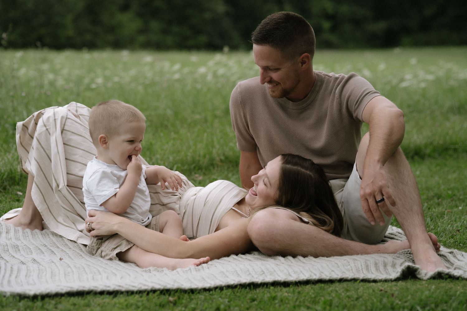 Family relaxing together on a blanket in the grass.