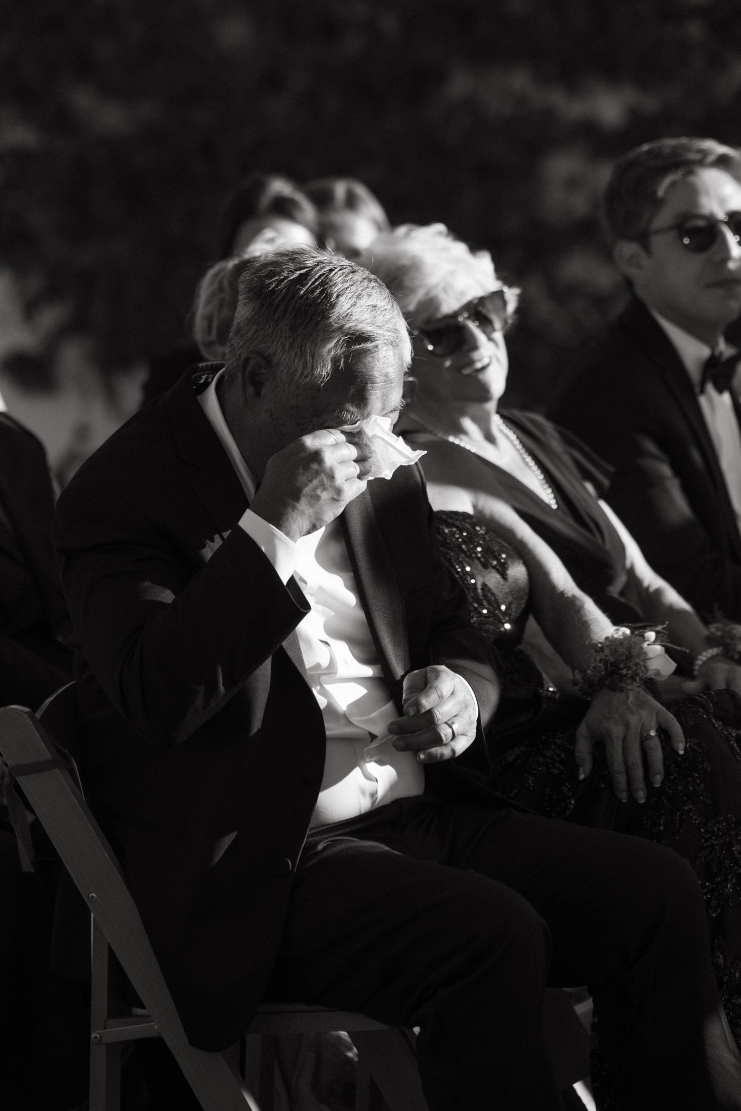 Guests in formal attire seated outdoors at an elegant event in black and white.
