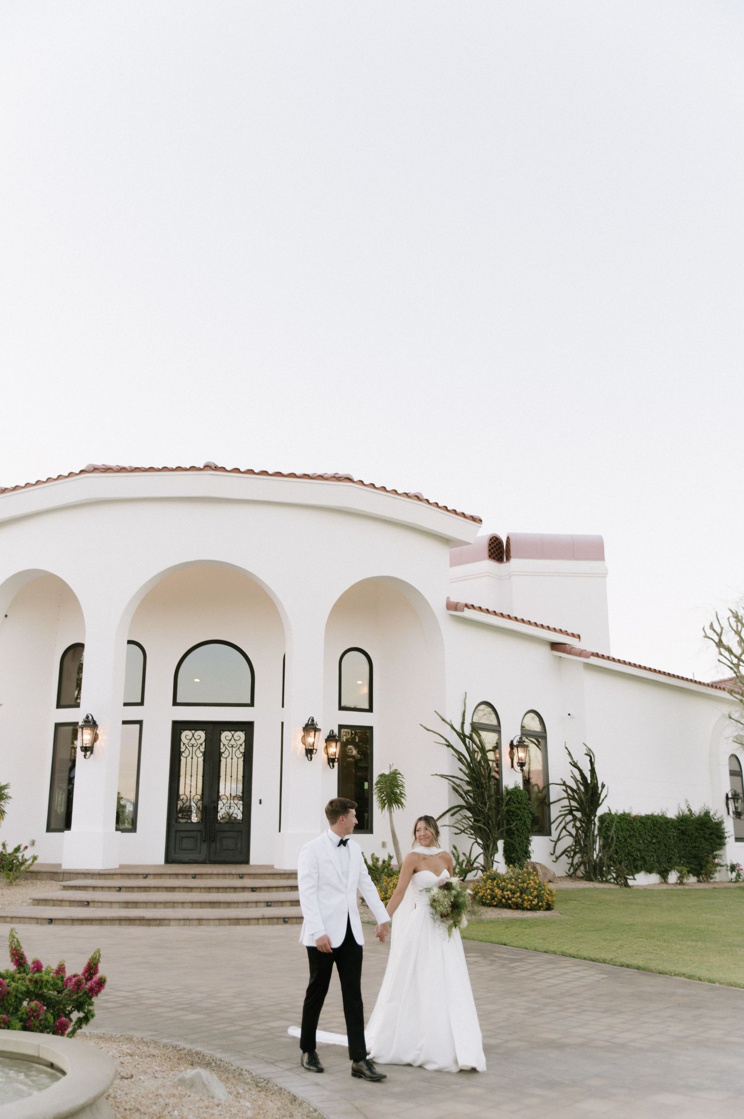 Elegant white Spanish-style wedding venue with arched windows and palm trees.
