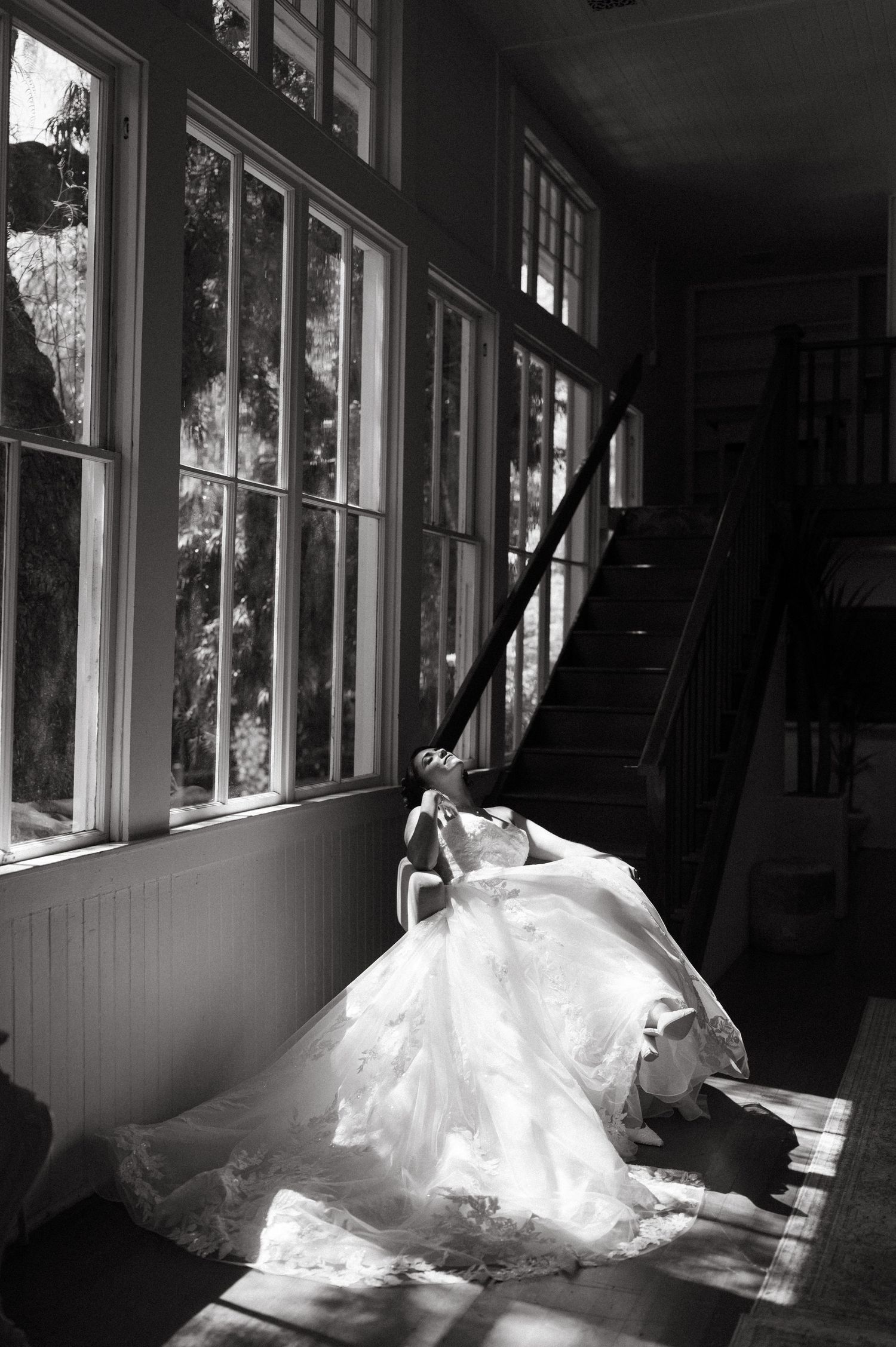 Dramatic black and white photo of a wedding dress in sunlit hallway with large windows.