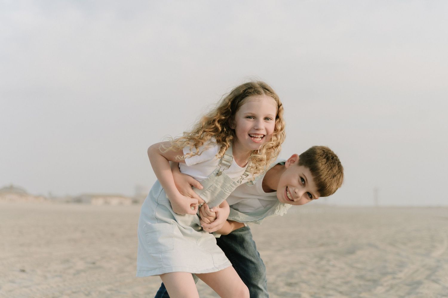 Playful family members laugh and tumble together on sandy beach.