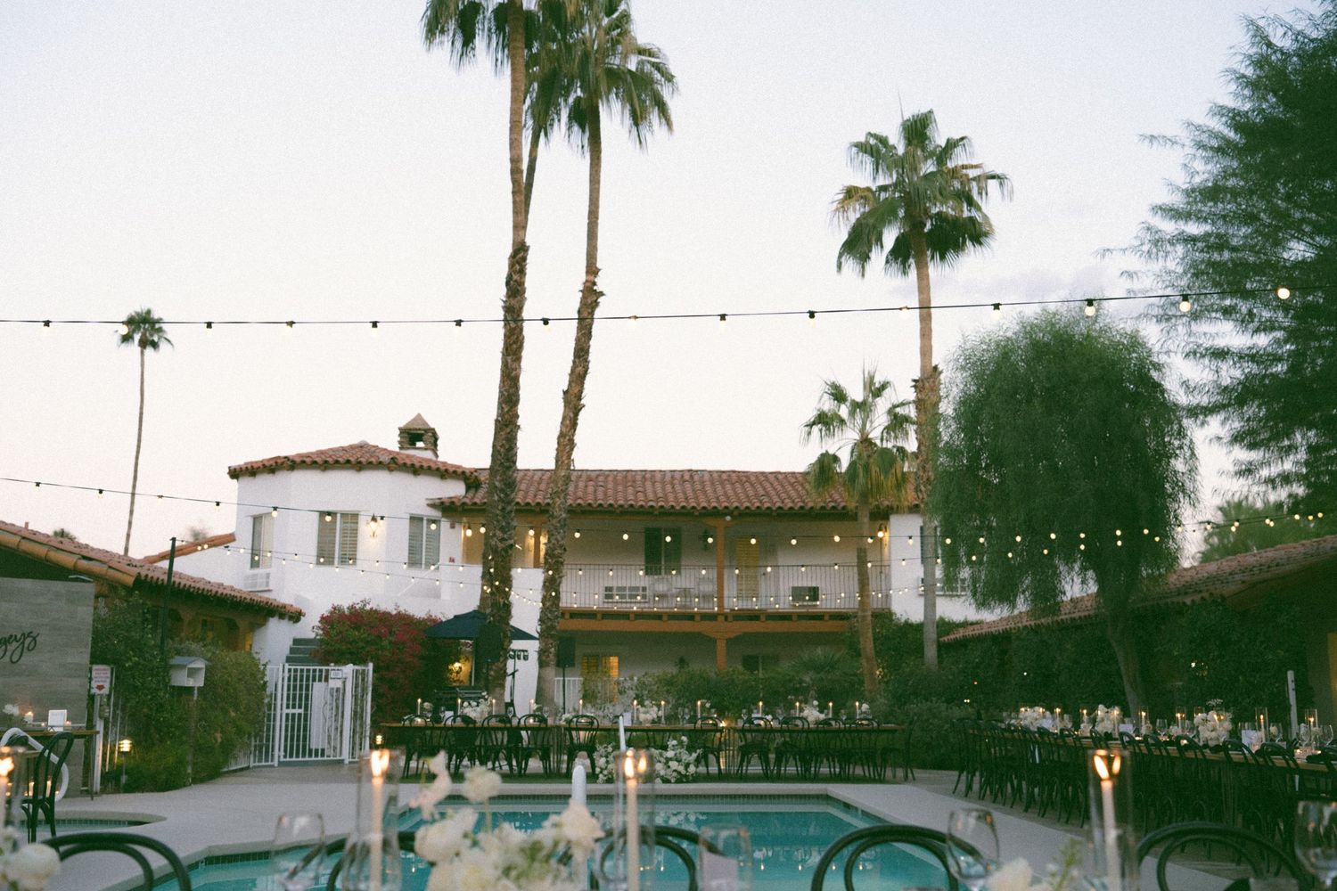 Palm trees and string lights create an ambiance at a desert venue at dusk.