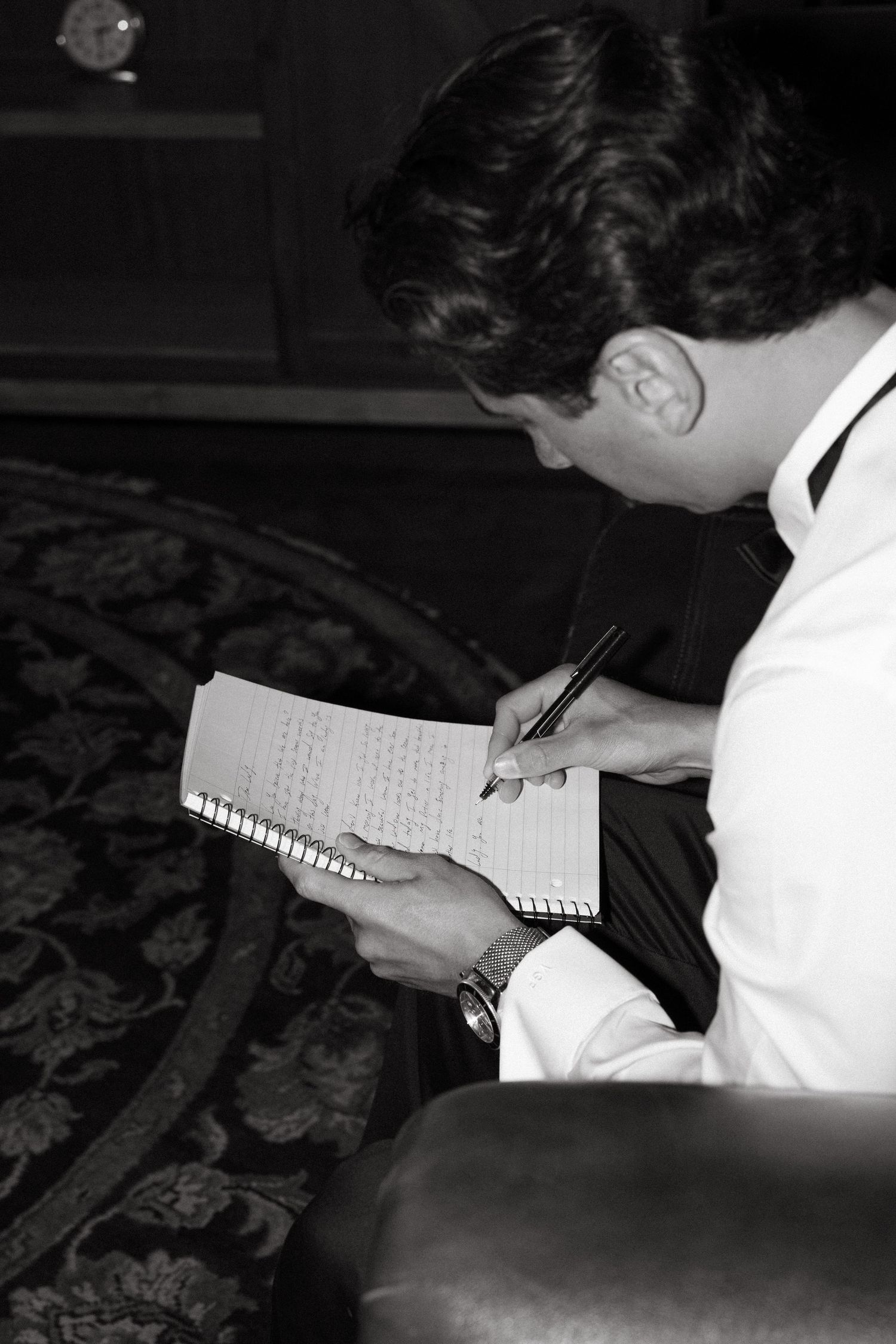 Black and white photo of someone writing in a notebook while seated.