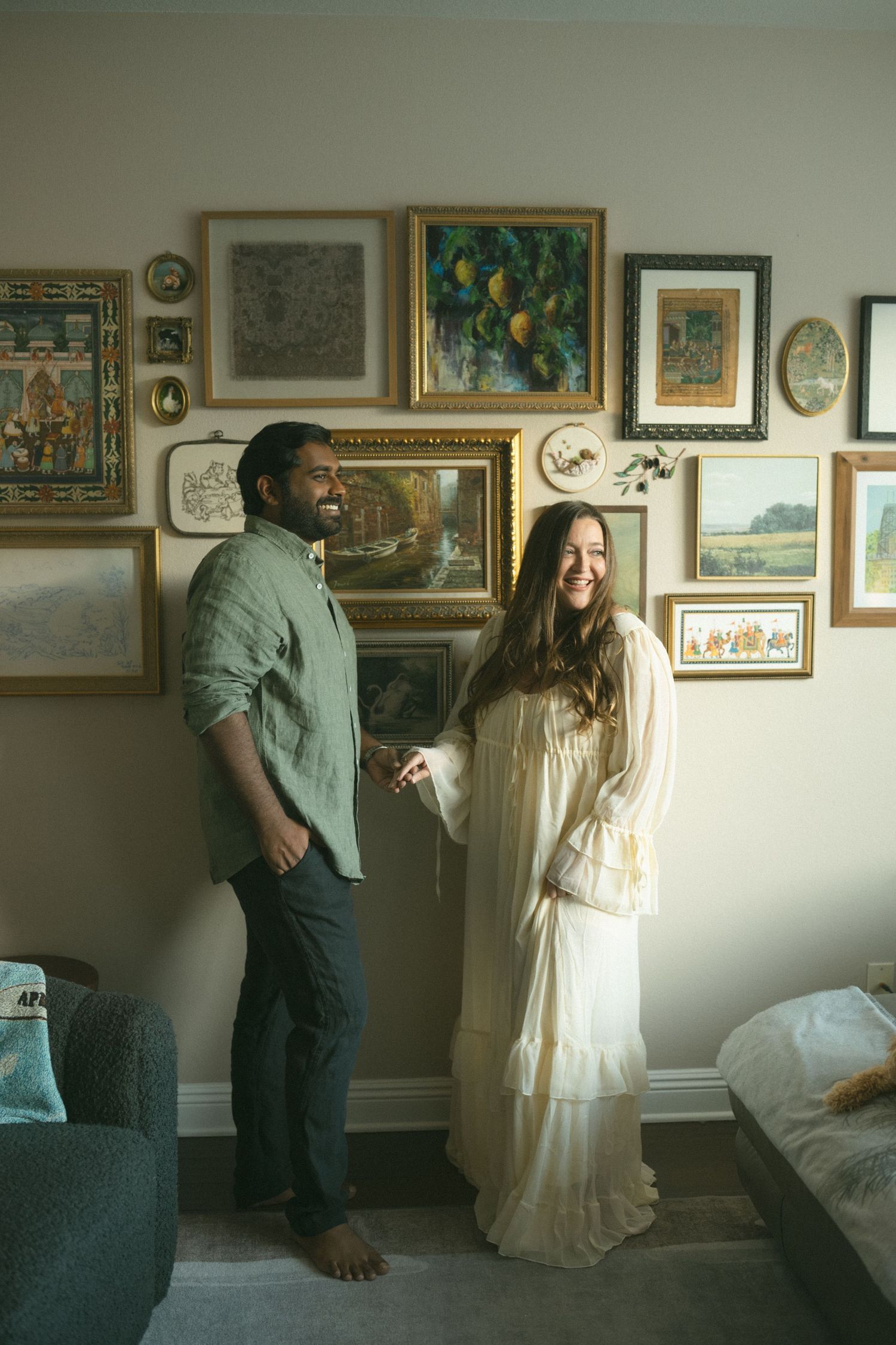 A couple poses in a room with walls covered in framed artwork and paintings.