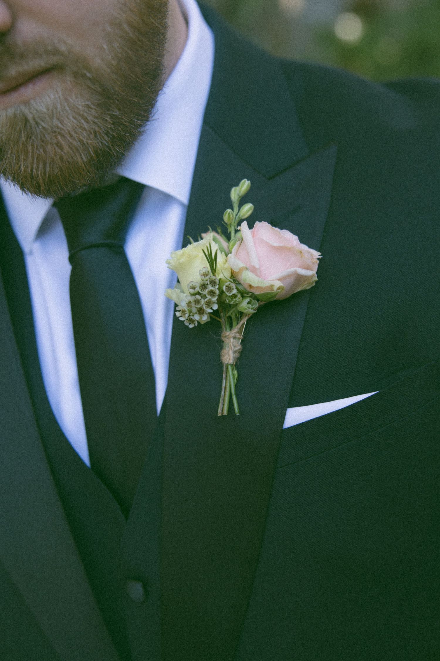 Close-up detail of a pink rose boutonniere on a black suit lapel.