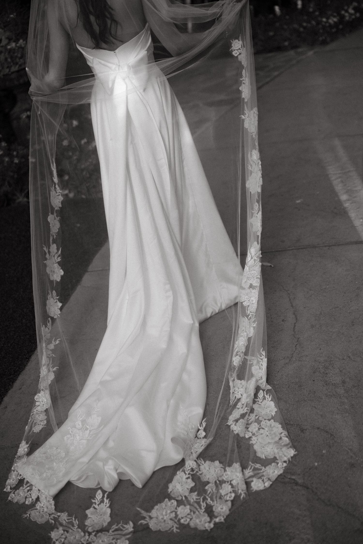 Detail shot of an elegant lace-trimmed wedding veil flowing on concrete in black and white.