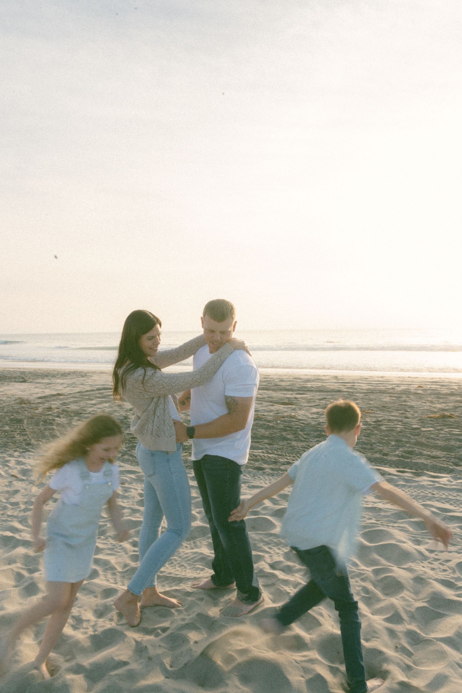 Family playing and dancing together on sandy beach at sunset.