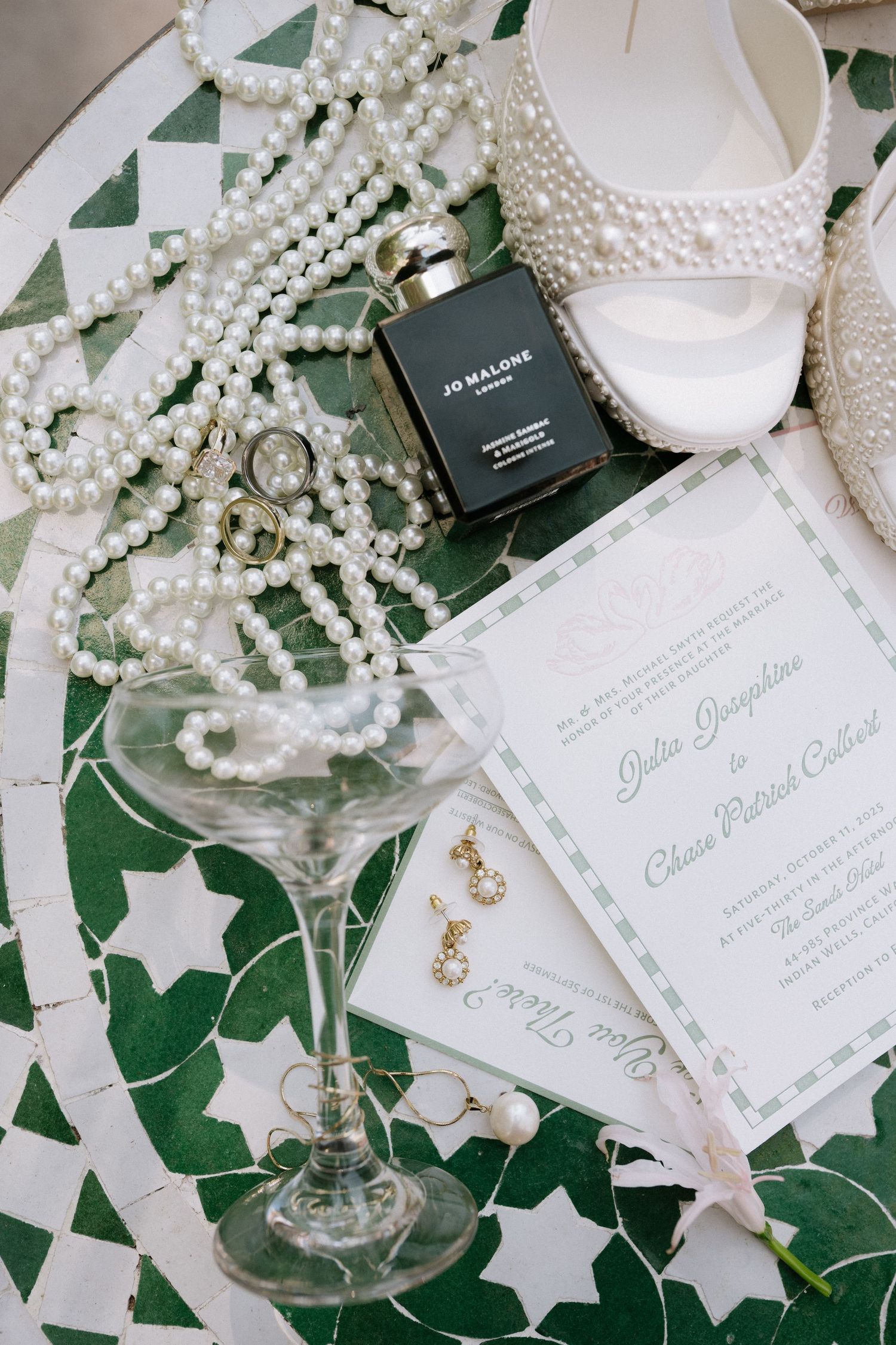 Elegant wedding details with pearls, invitations and accessories on green background.