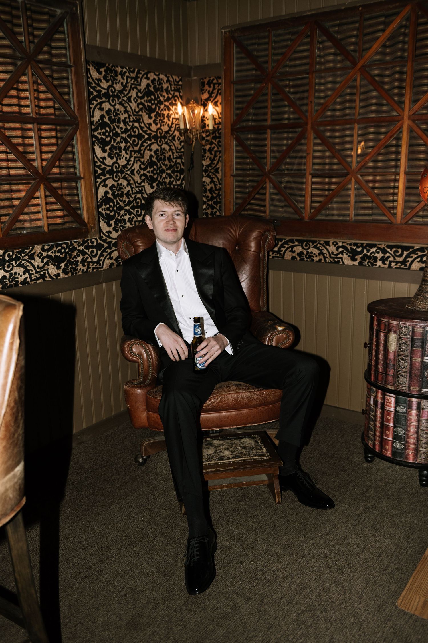 Classic formal portrait in an elegant room with leather chair and decorative wallpaper.