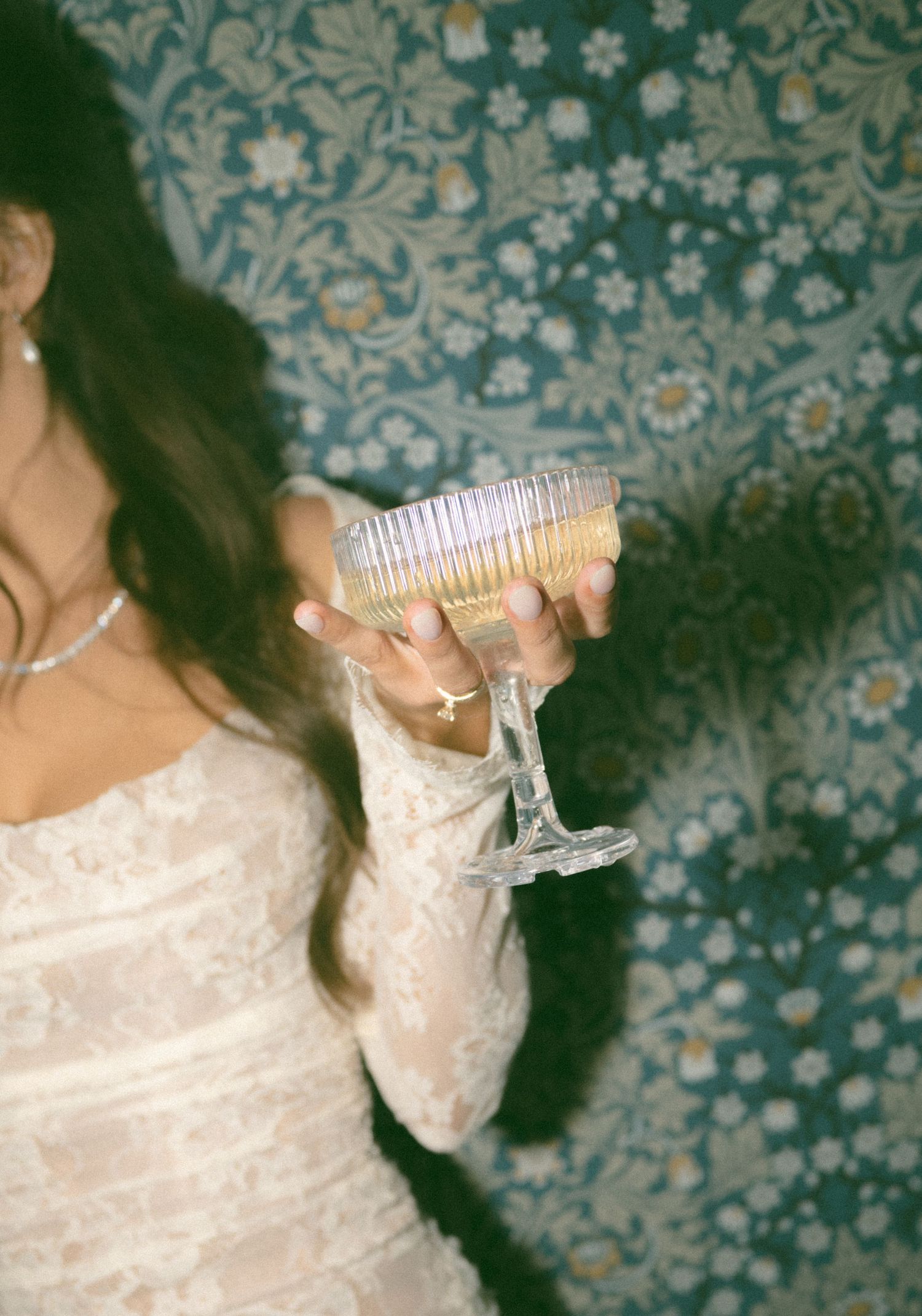 Close-up of champagne glasses held by someone wearing a lace wedding dress sleeve.