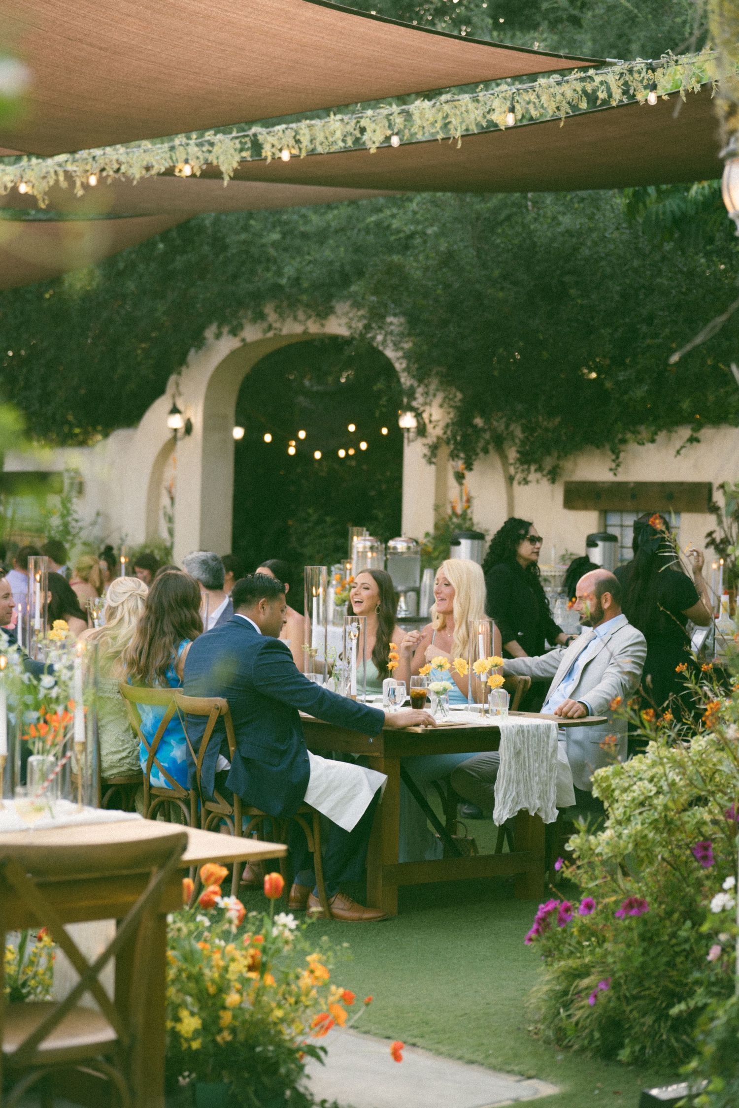 Garden wedding reception with string lights, floral decorations and guests dining at tables.