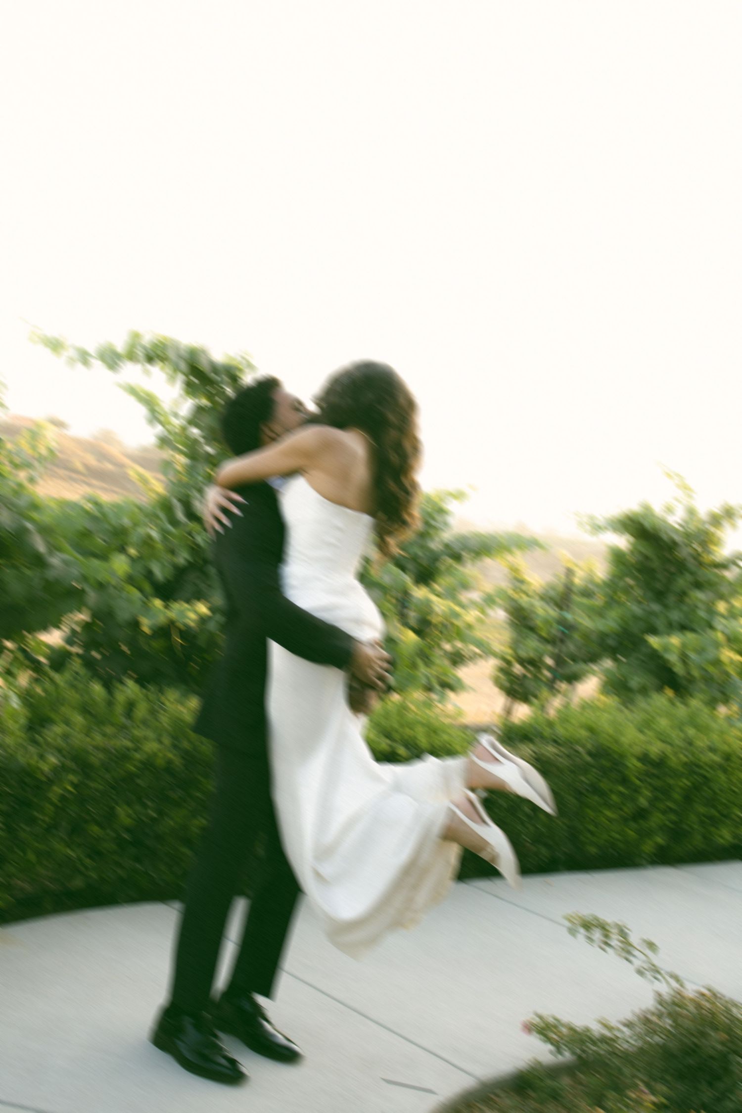 Motion-blurred photo of couple in wedding attire spinning in an embrace outdoors.