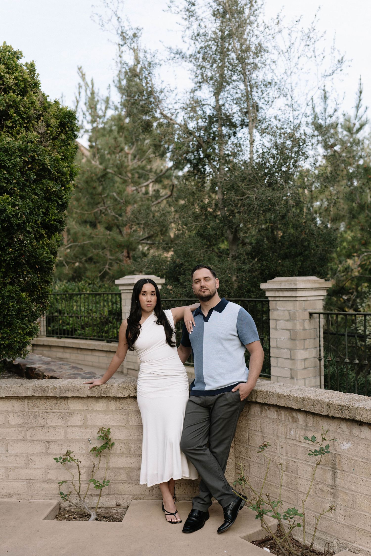 Couple sitting together on a stone wall surrounded by lush greenery.