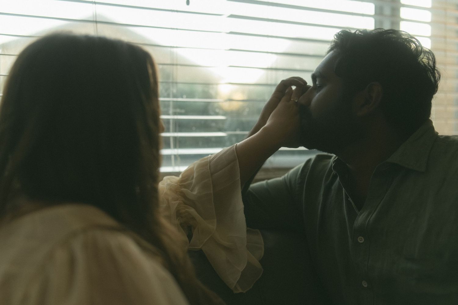 Silhouettes of people sitting by a window with sunlight streaming through blinds.