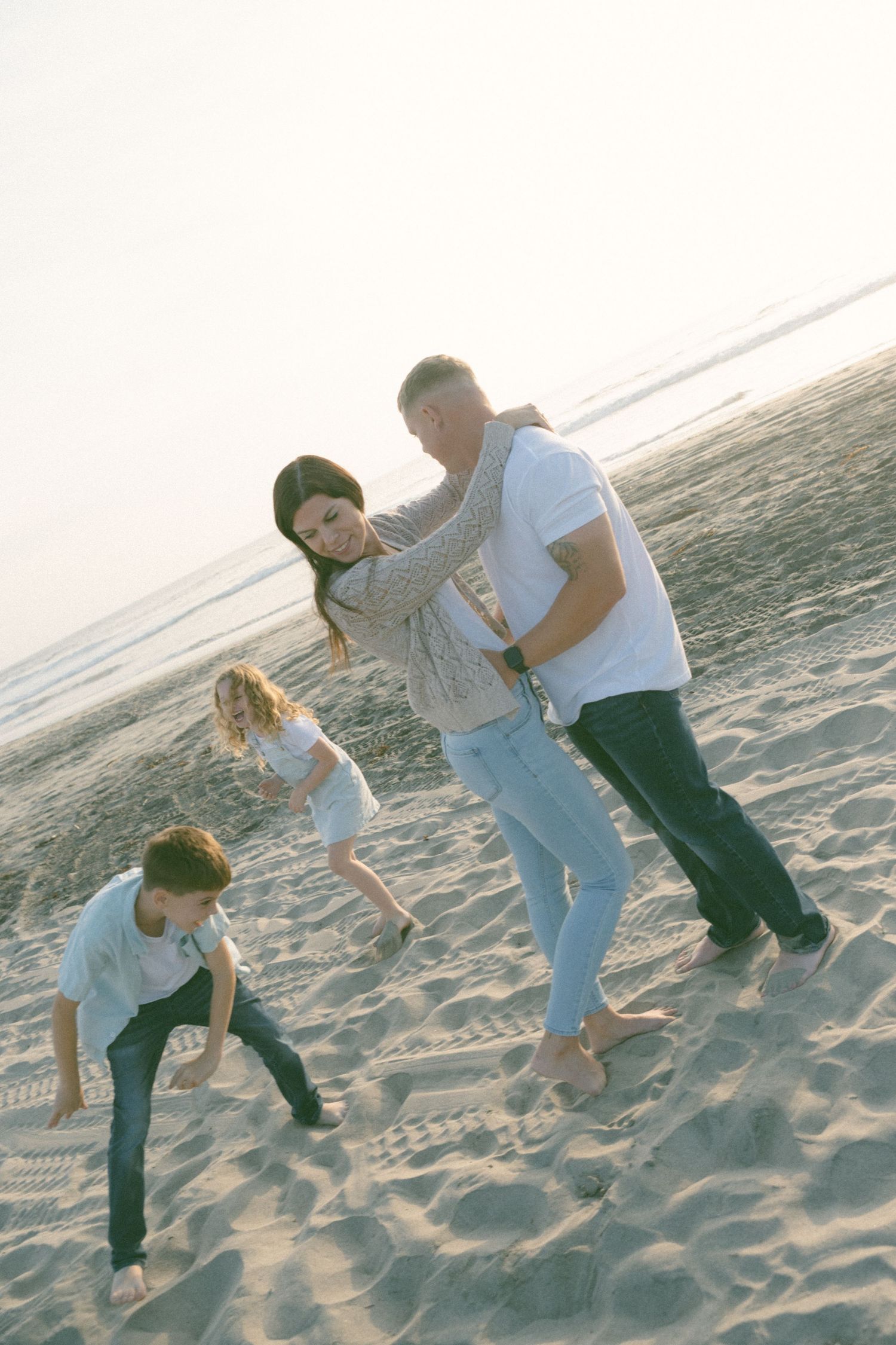 Family members play and kick sand together on a sunny beach.
