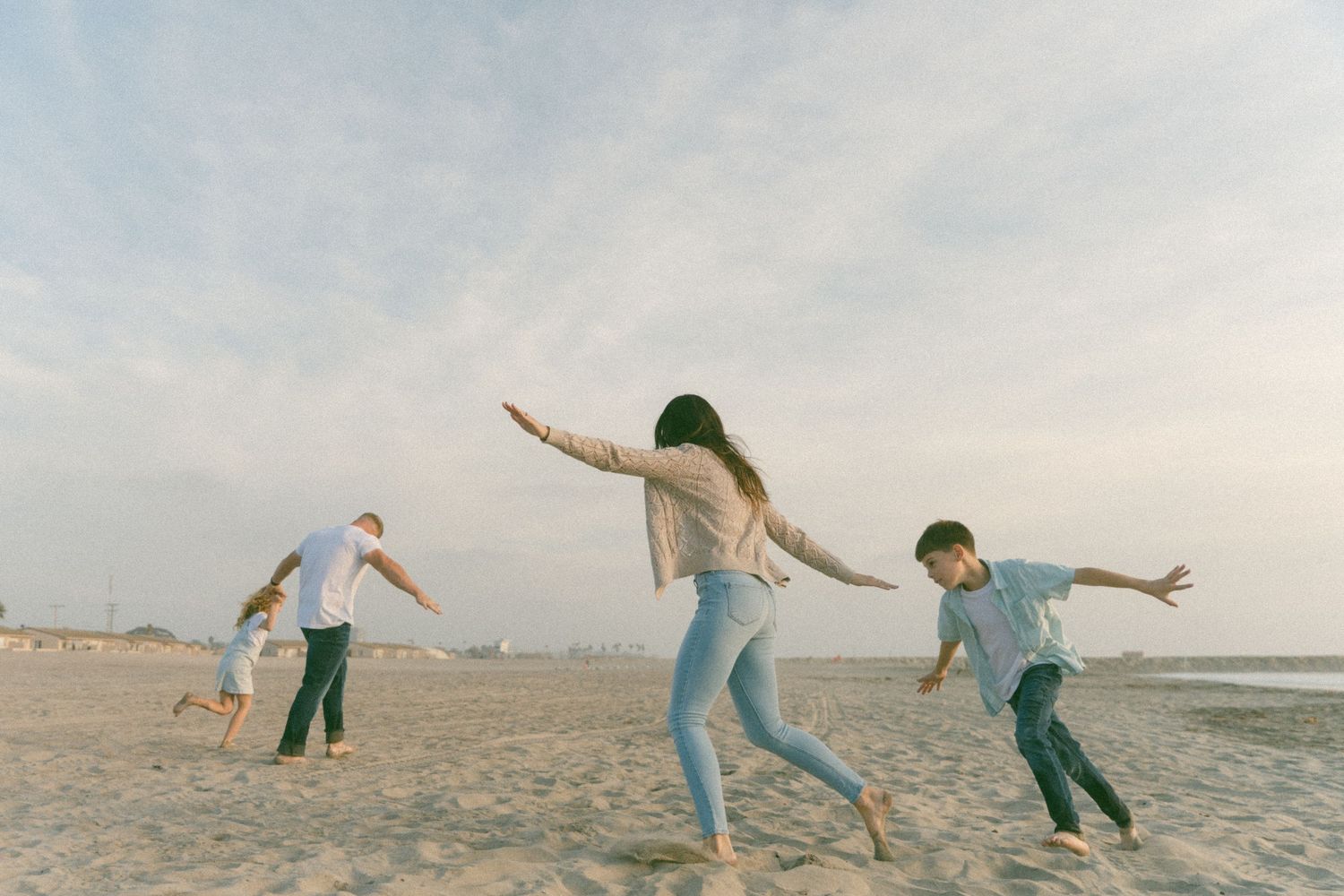 Family members lean and balance playfully on the beach during sunset.