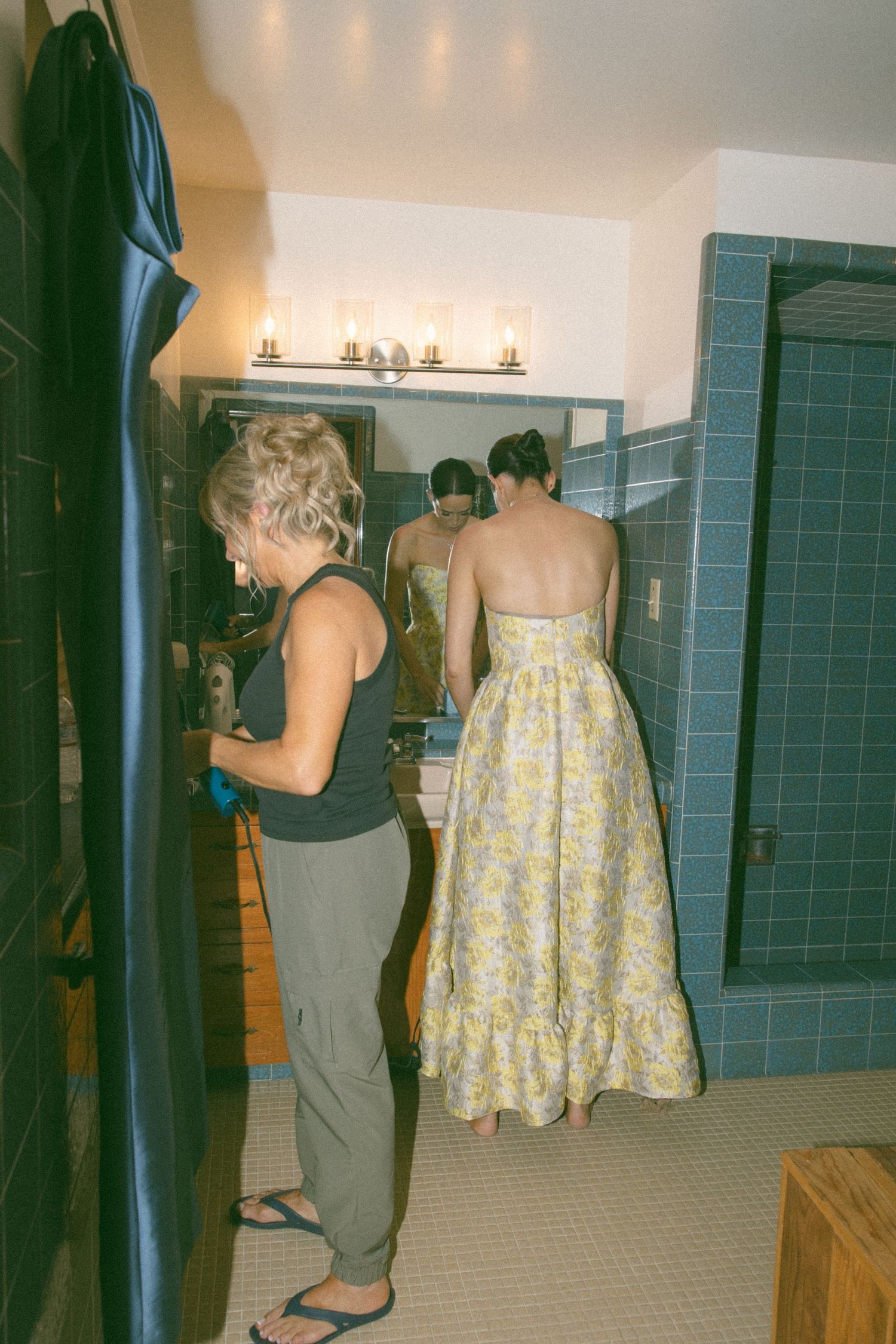 Behind-the-scenes moment in a bathroom with blue tile and yellow floral dress.