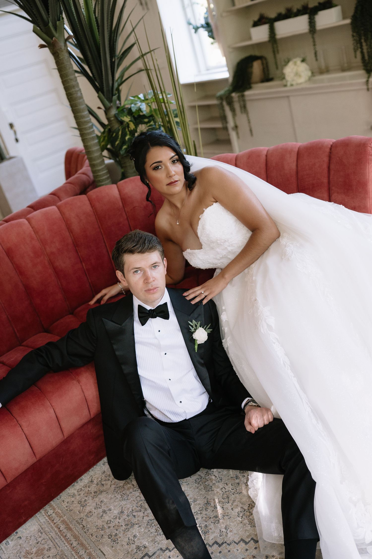Wedding couple posing on a vintage red velvet couch in formal attire.