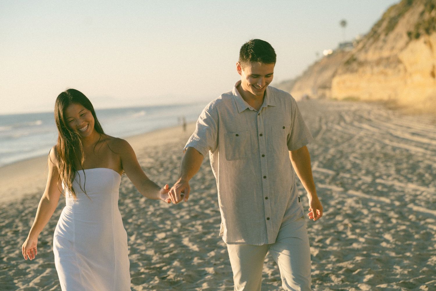People walking along a beach with golden sunlight and cliffs in the background.