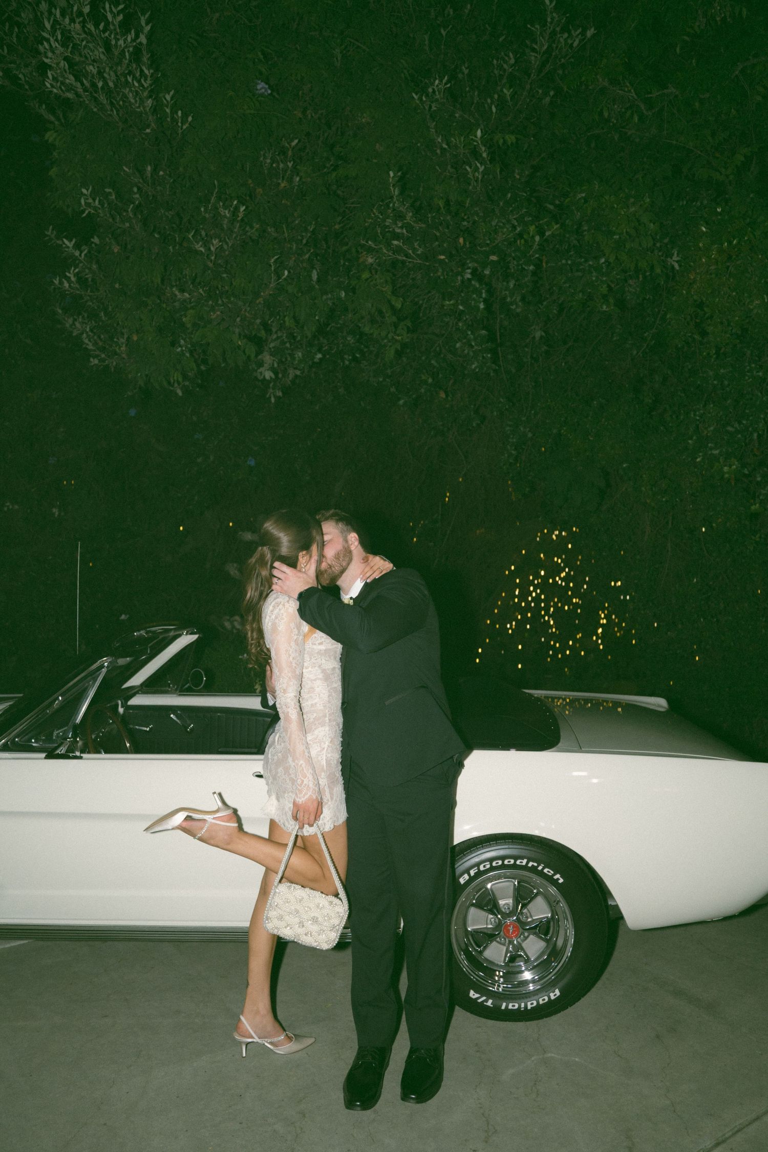 Romantic nighttime portrait of newlyweds embracing next to a classic white car.