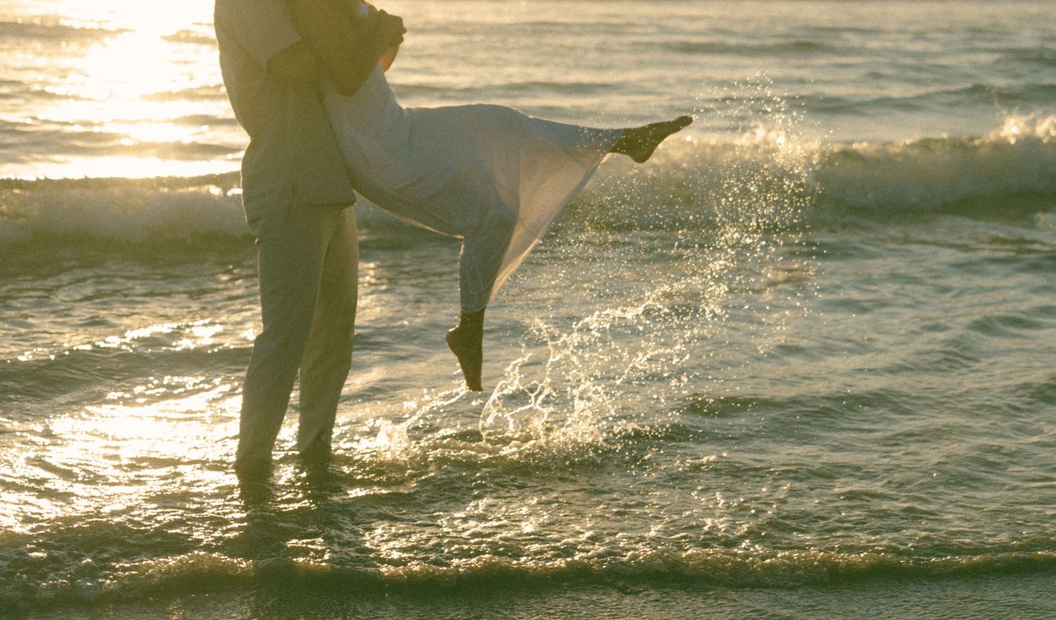 Silhouettes of people playing and splashing in ocean waves at sunset create a joyful beach scene.