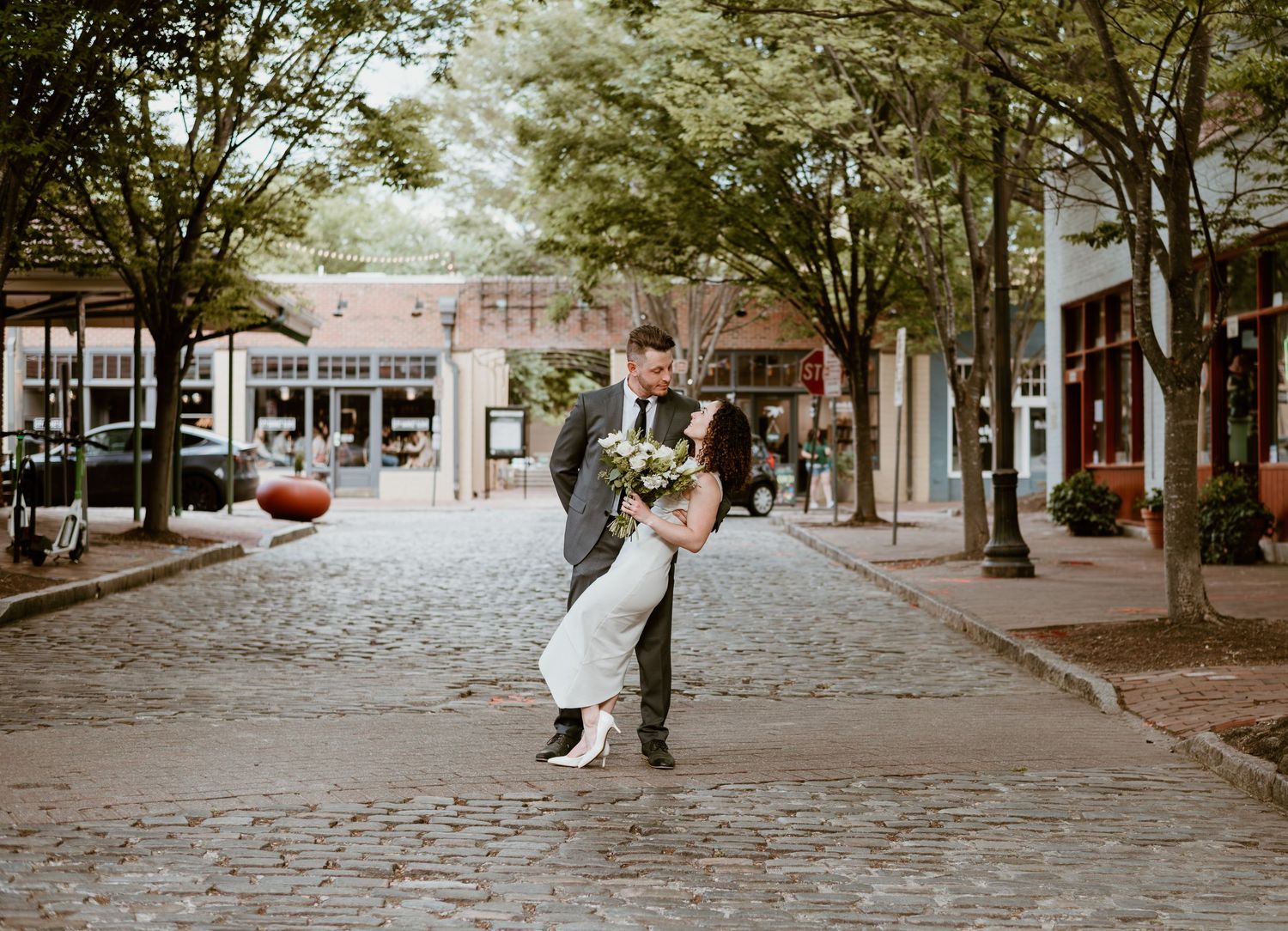 A couple embraces on a charming cobblestone street lined with shops and autumn decorations in a historic village.
