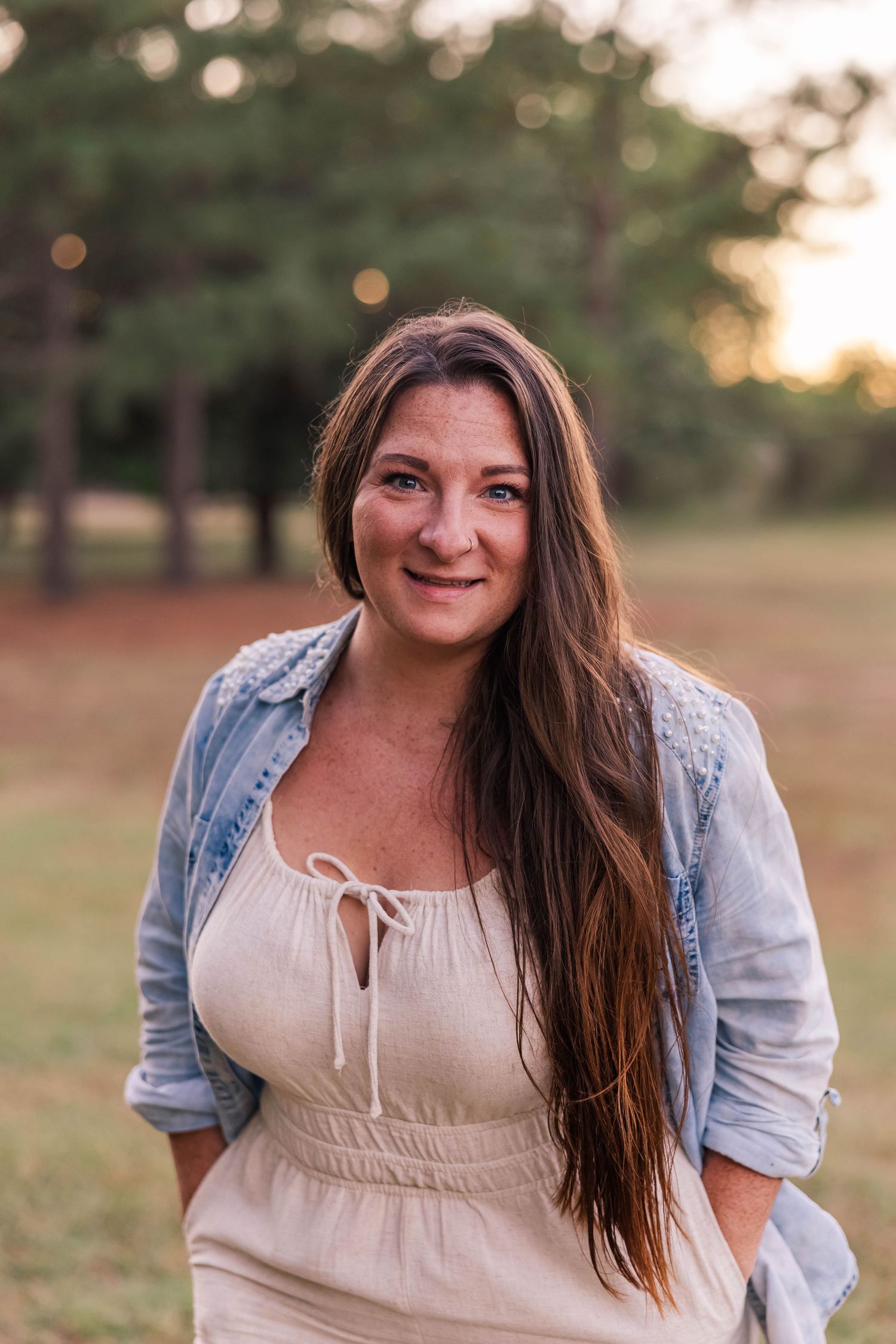 Woman in casual attire smiles warmly during golden hour outdoor photoshoot.