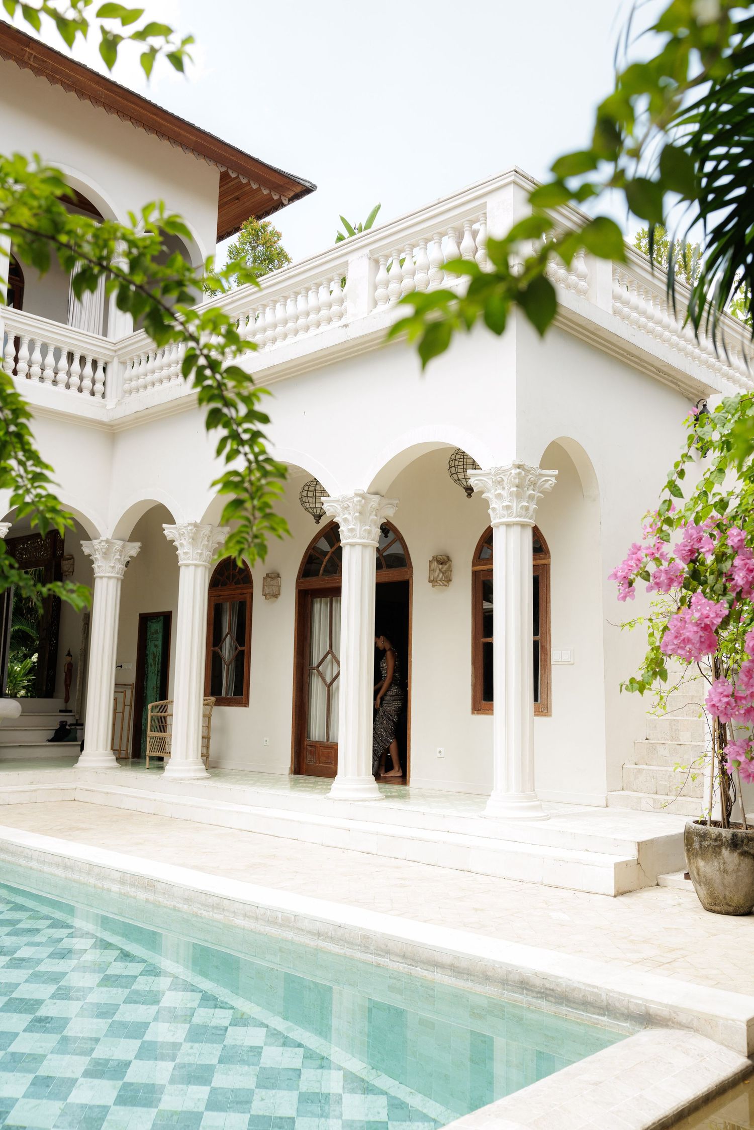 Elegant white villa with arched colonnade, ornate columns, and turquoise pool surrounded by greenery.