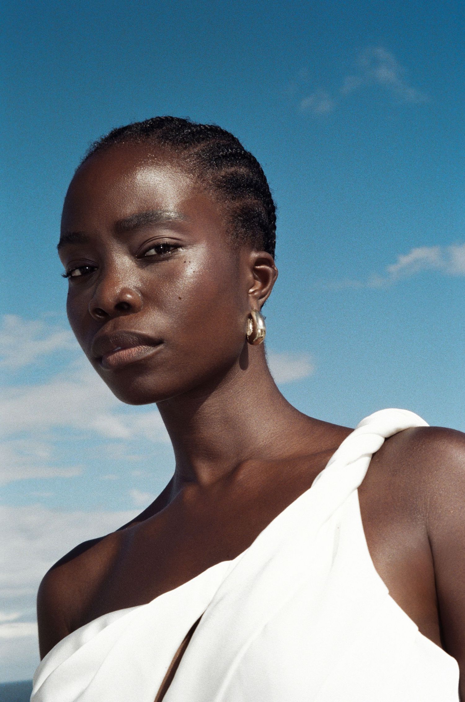 Portrait of a beautiful Black bride in white one-shoulder dress against blue sky backdrop.