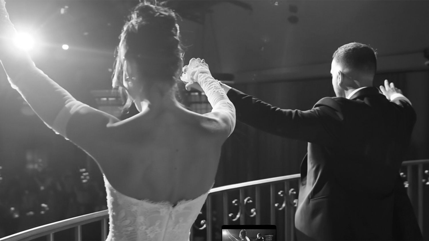 Black and white photo of bride and groom dancing energetically on illuminated wedding dance floor.