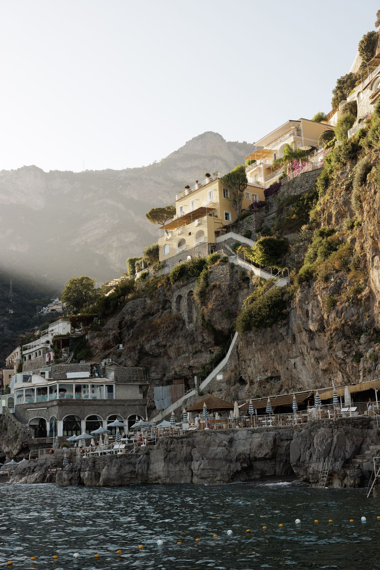 Cliffside buildings and terraces overlooking the sea on the Amalfi Coast at sunset.