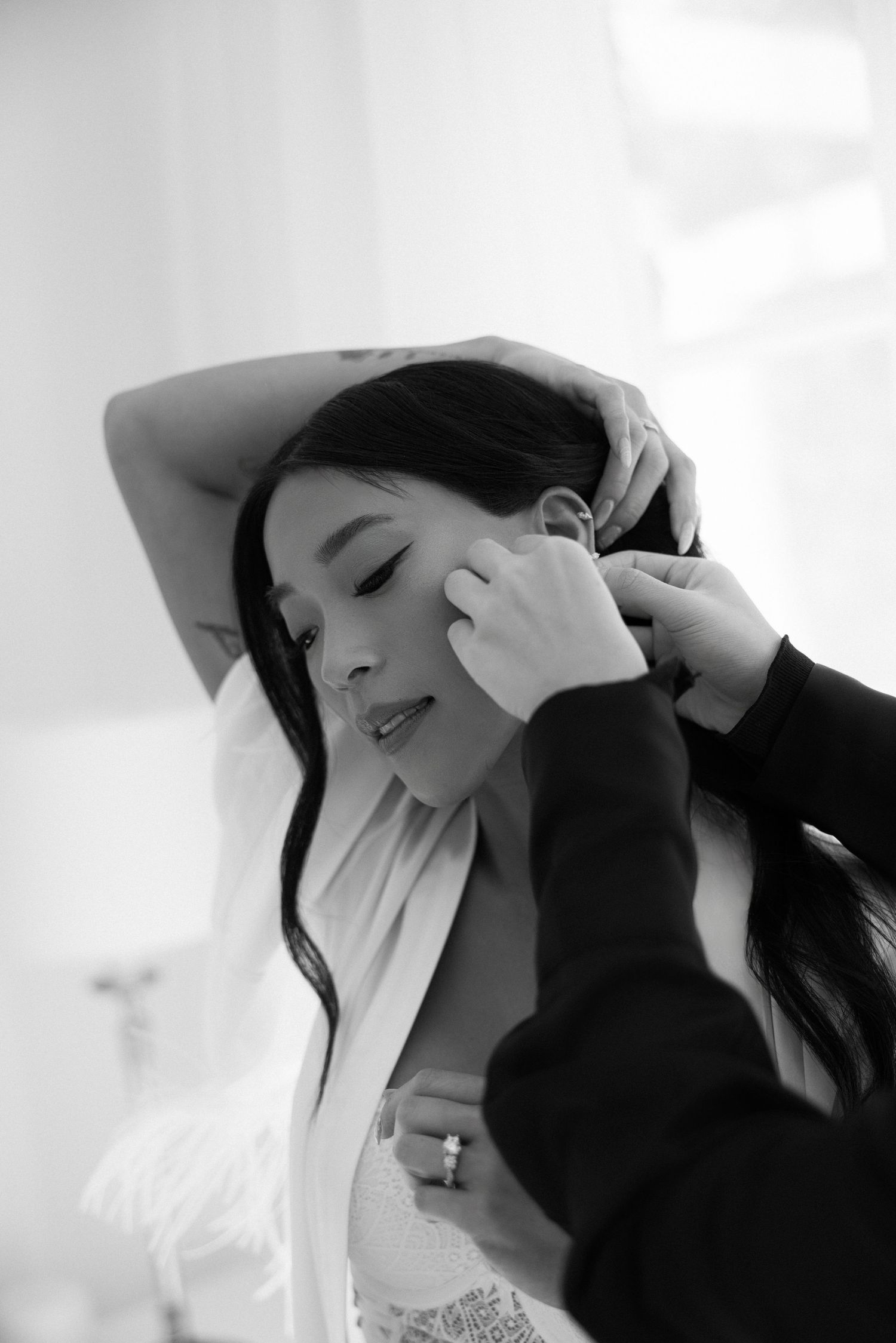 Black and white portrait of Asian bride having earrings put on during wedding preparations.