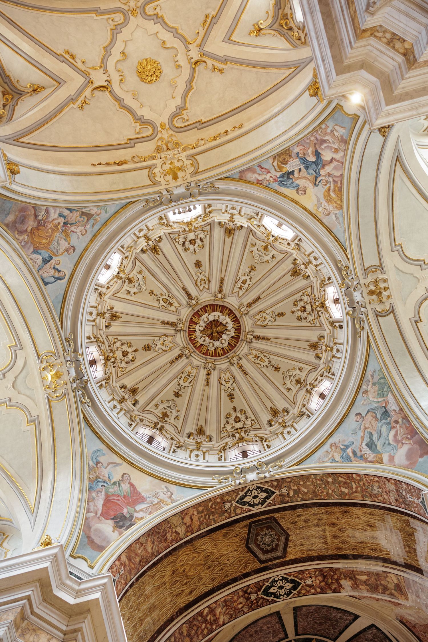 Ornate baroque church ceiling with gilded dome, frescoes, and decorative gold details.