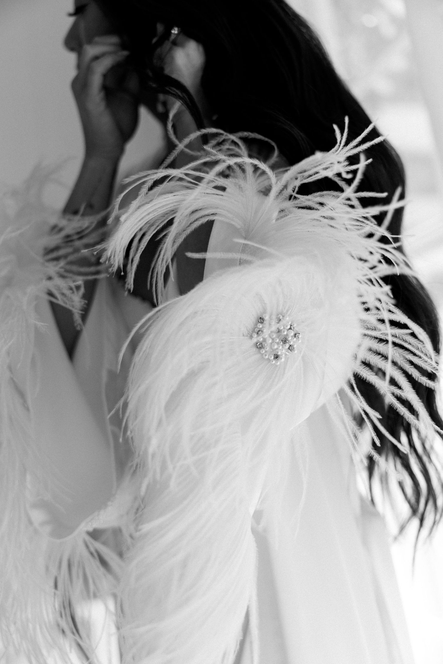 Close-up black and white detail of white feathered bridal robe with crystal brooch.