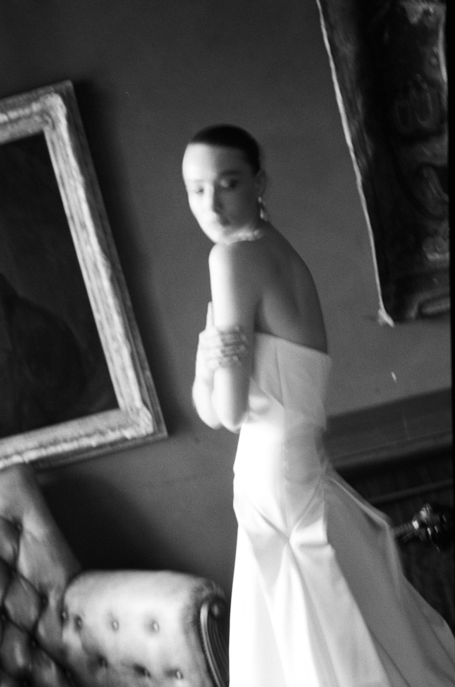 Black and white artistic photo of bride in strapless white wedding gown in ornate room.