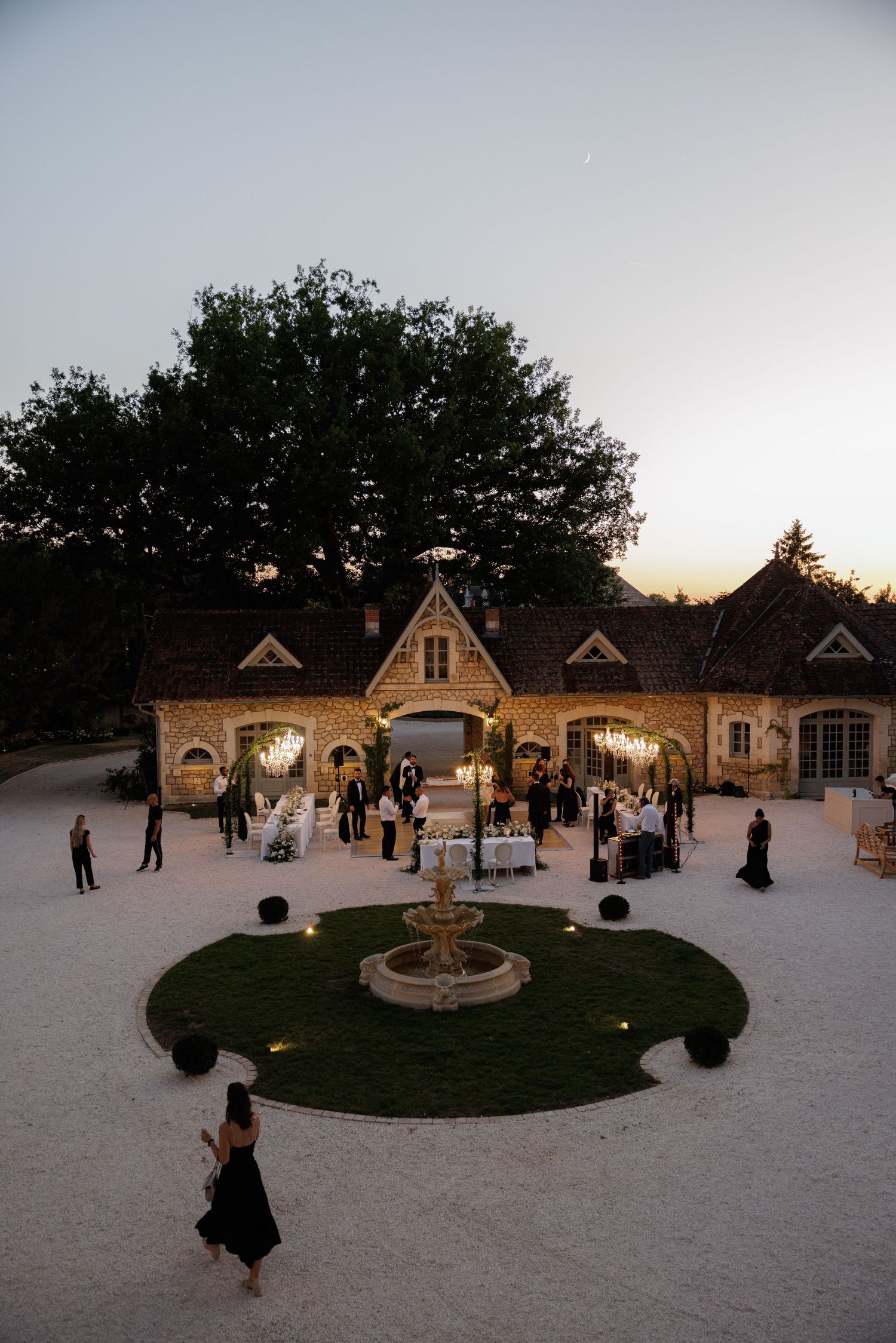Aerial view of elegant chateau wedding reception at dusk with fountain courtyard.